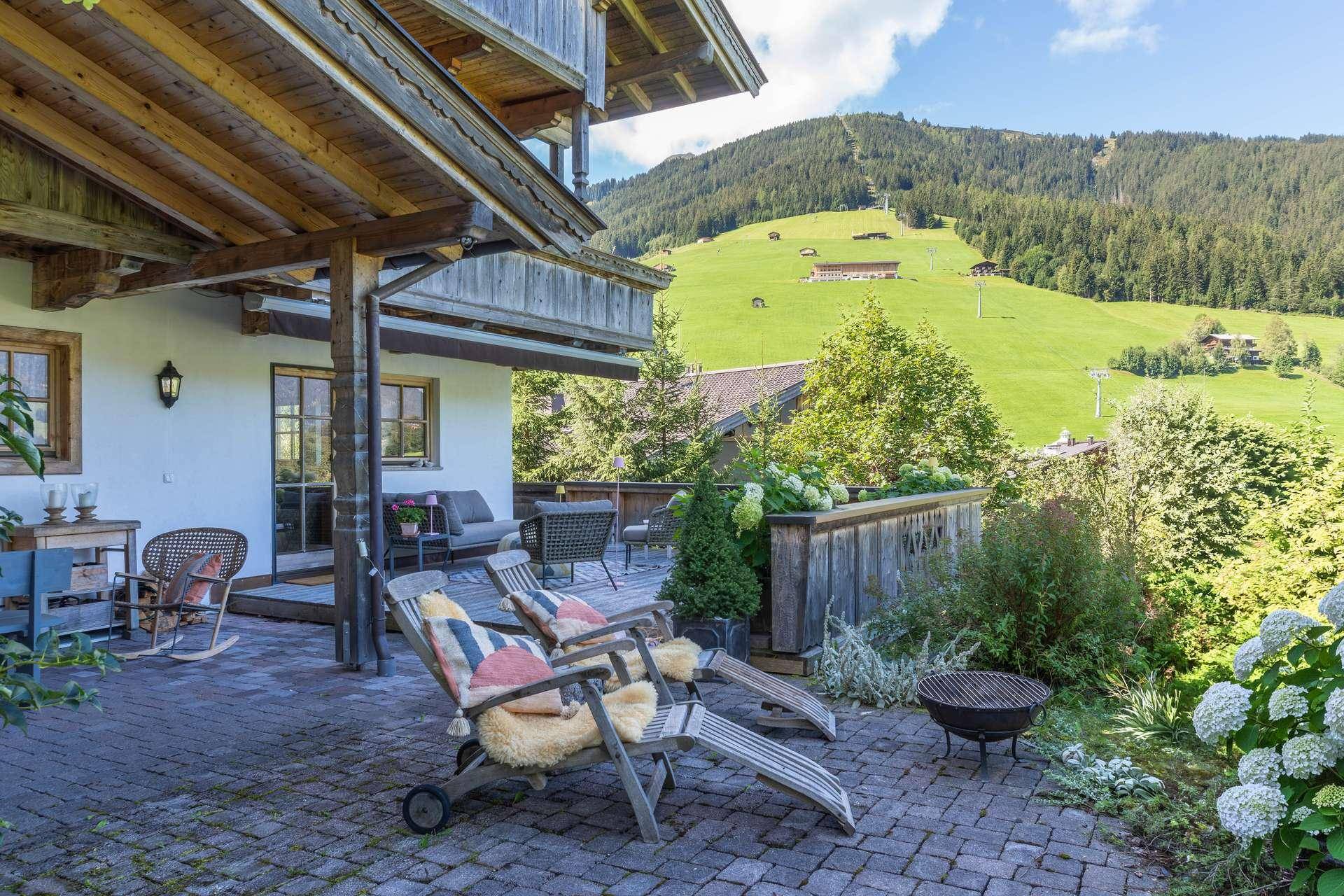 Gemütliche gepflasterte Terrasse mit Liegestühlen und Feuerstelle, umgeben von üppiger Bepflanzung.