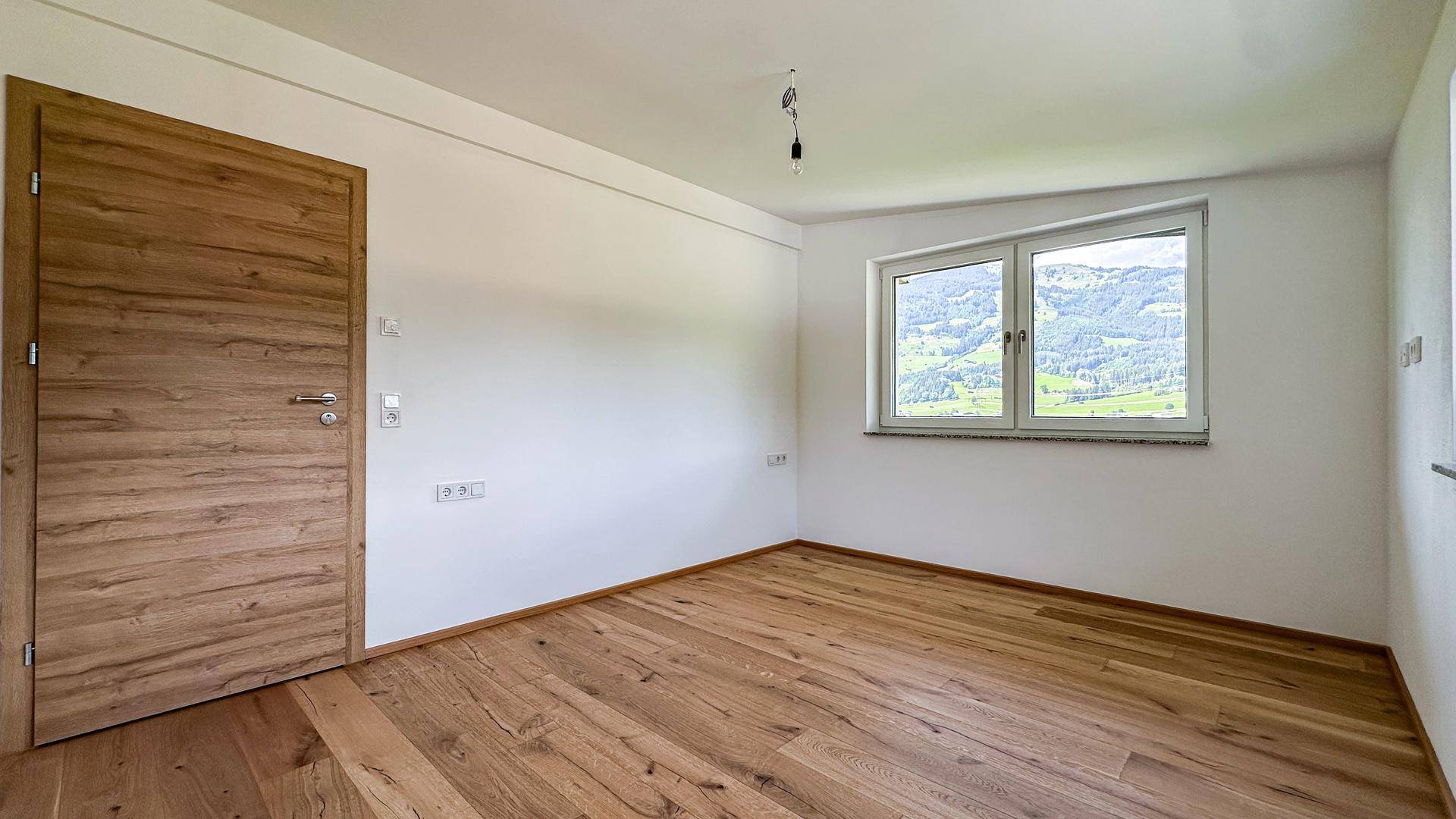 Leeres Schlafzimmer mit Holzboden, weiß gestrichenen Wänden und einem Fenster mit Bergblick.