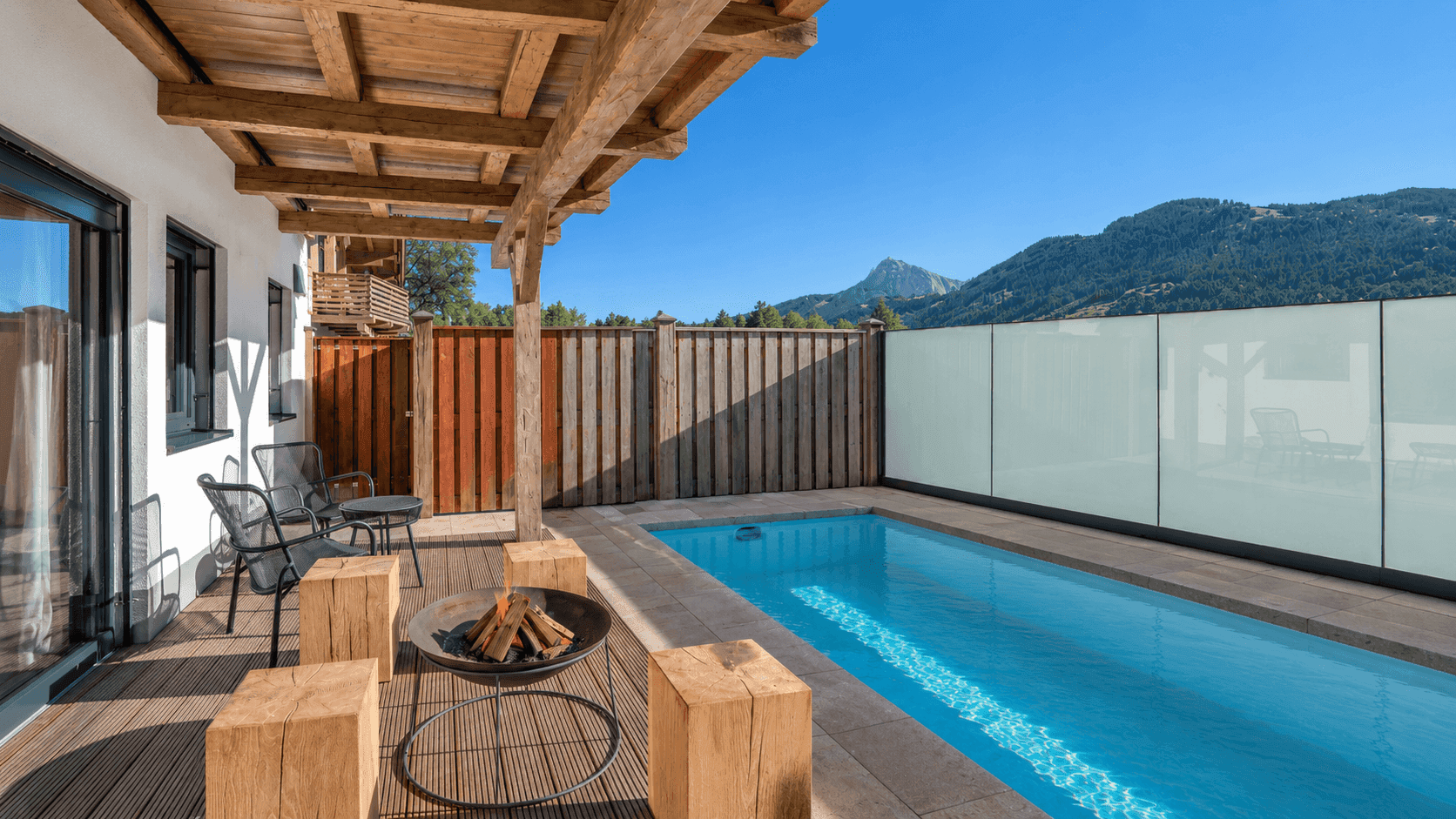 Moderne Terrasse mit kleinem Pool, Feuerstelle und Bergblick in sonniger Umgebung.
