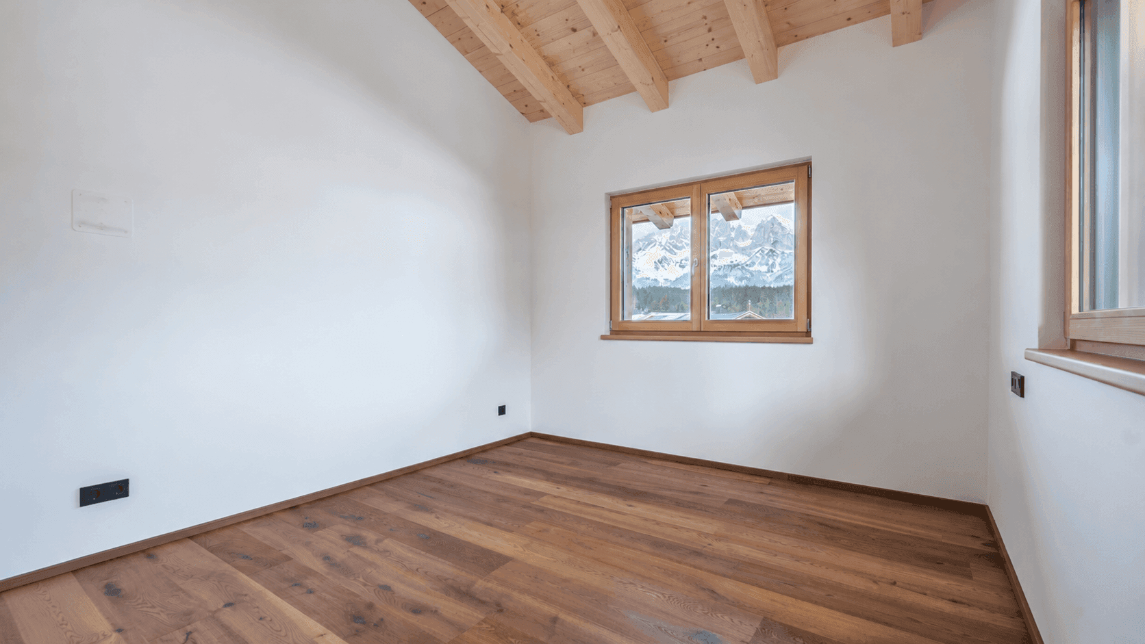Helles Zimmer mit Holzboden, Holzbalkendecke und Fenster mit Bergblick.
