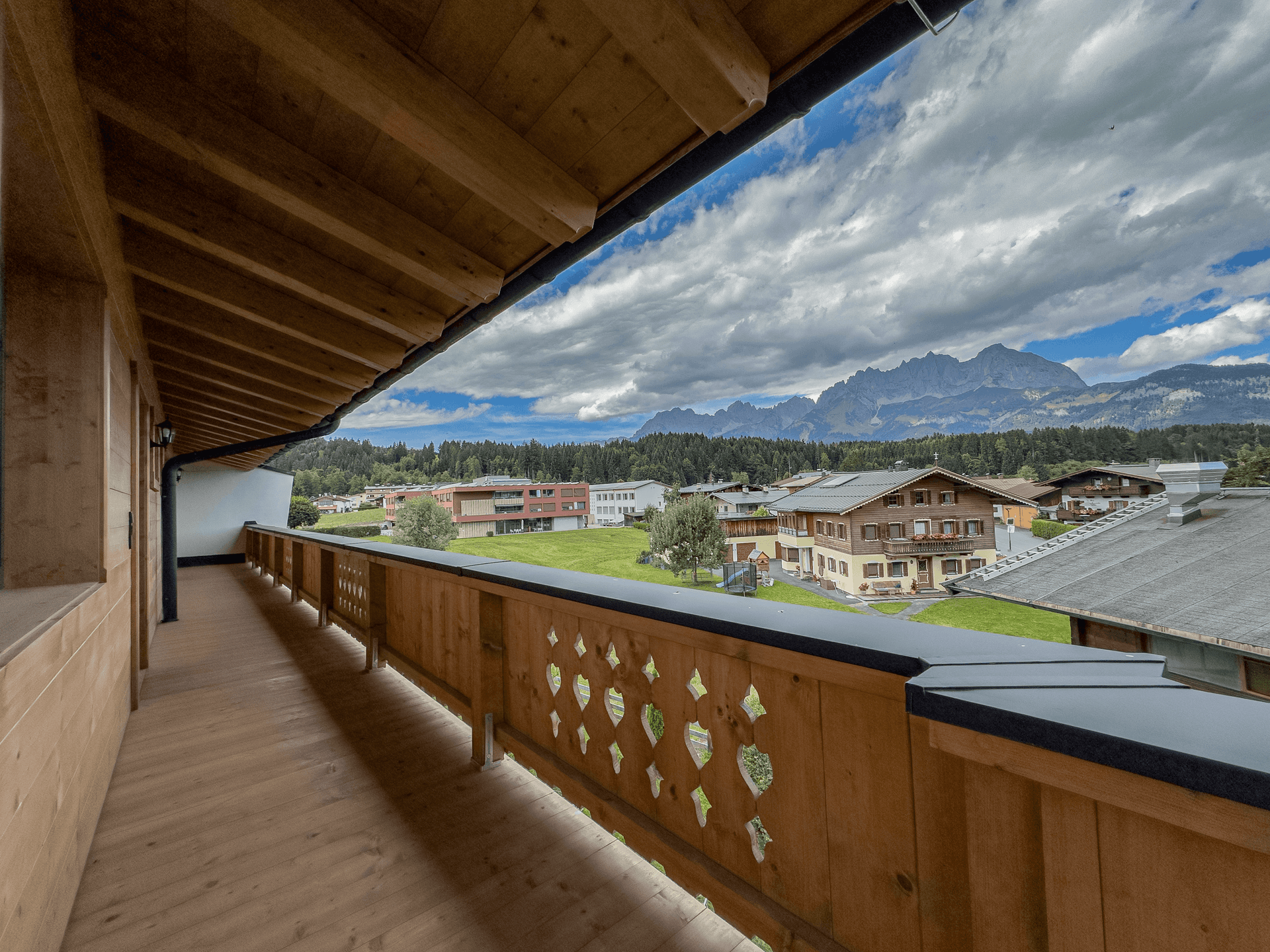 Langer Holzbalkon mit traditionellem Geländer und weitem Panoramablick auf die Berge und das Tal.