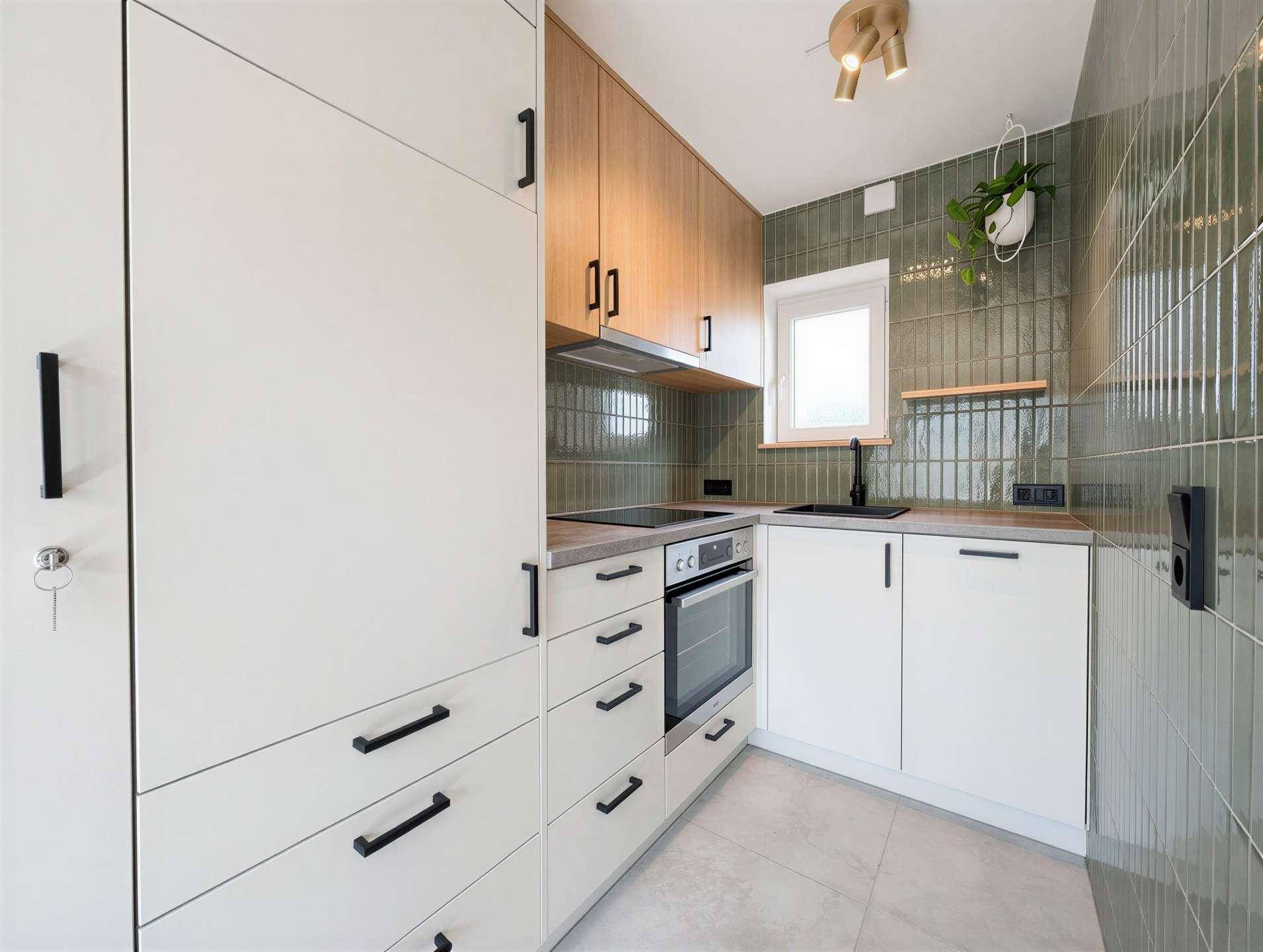Moderne Küche mit weißen Schränken, Holzdetails und grünen Fliesen an der Wand.