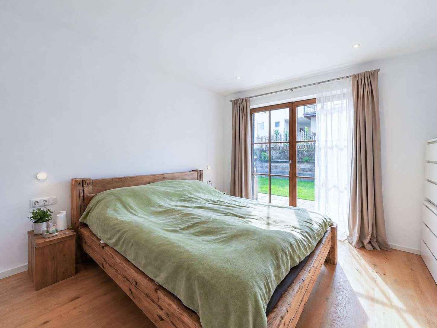 Gemütliches Schlafzimmer mit Holzbett, Parkettboden und direktem Zugang zum grünen Garten.