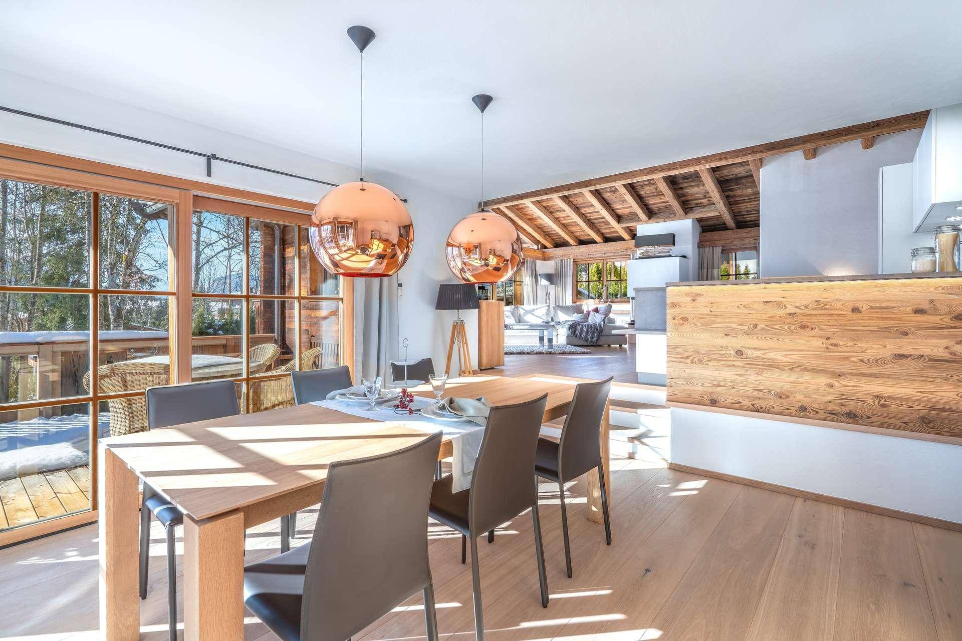 Heller Essbereich mit Holztisch, modernen Leuchten und Zugang zur Terrasse mit Bergblick.