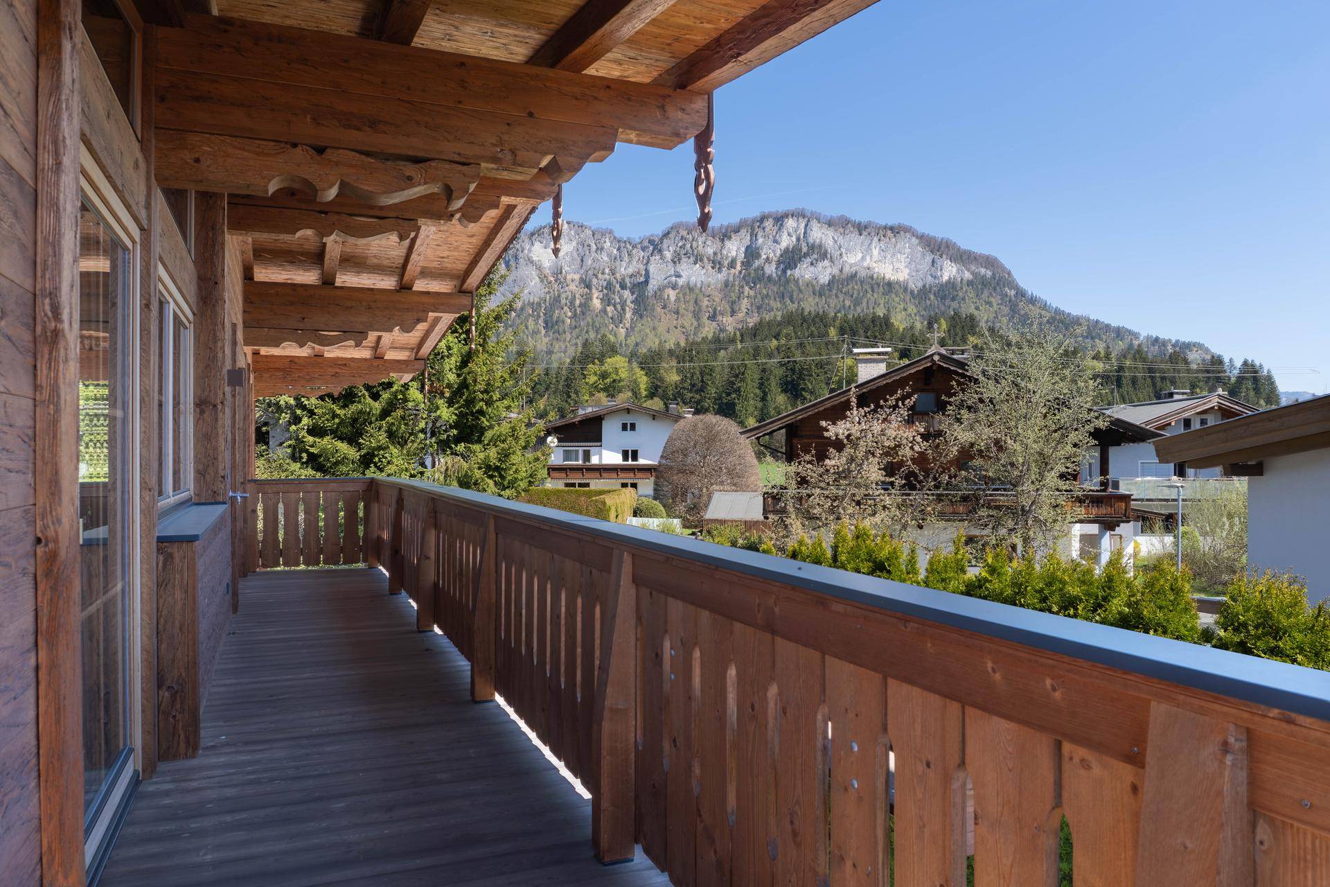 Langer Holzbalkon mit traditionellem Geländer und Panoramablick auf die Berge.