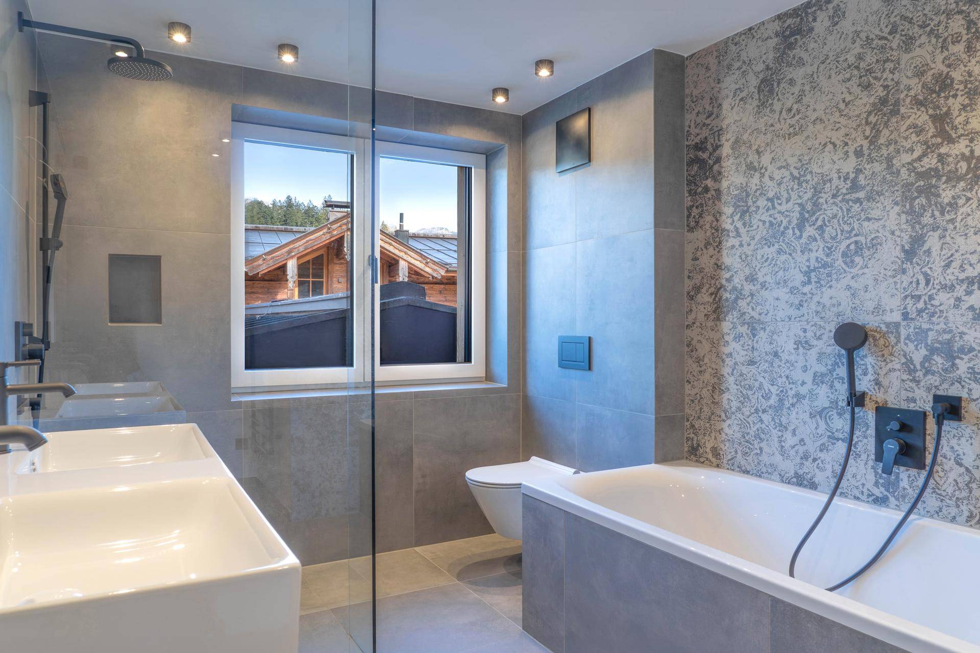 Modernes Badezimmer mit grauen Fliesen, Doppelwaschbecken, Badewanne und Fenster.