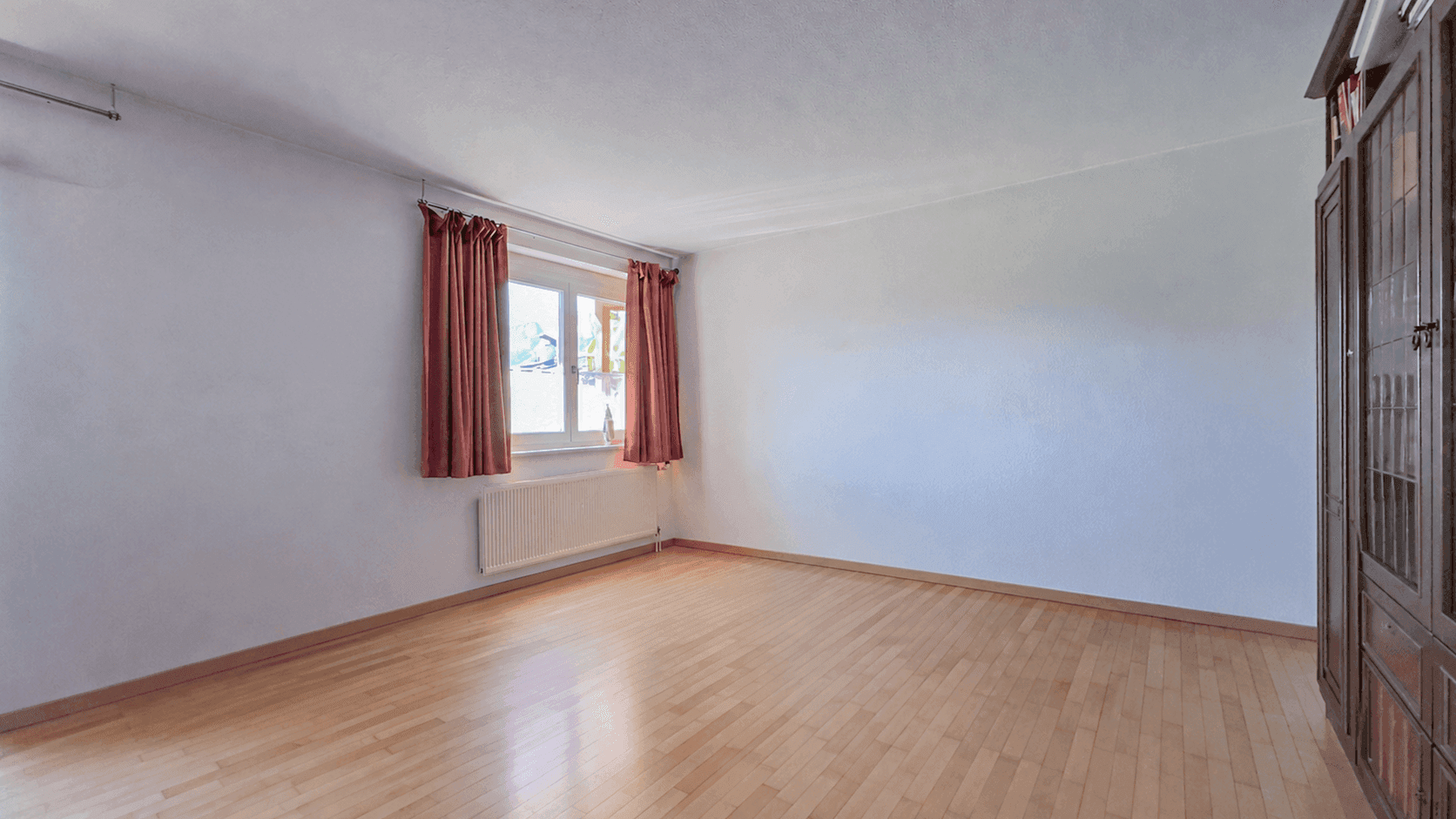 Lichtdurchfluteter Raum mit Parkettboden und großem Fenster, ideal als Wohn- oder Schlafzimmer.