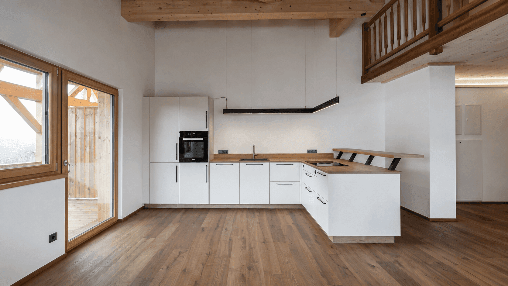 Moderne weiße Küche in offenem Wohnbereich mit Holzboden und Zugang zur Terrasse oder Balkon.