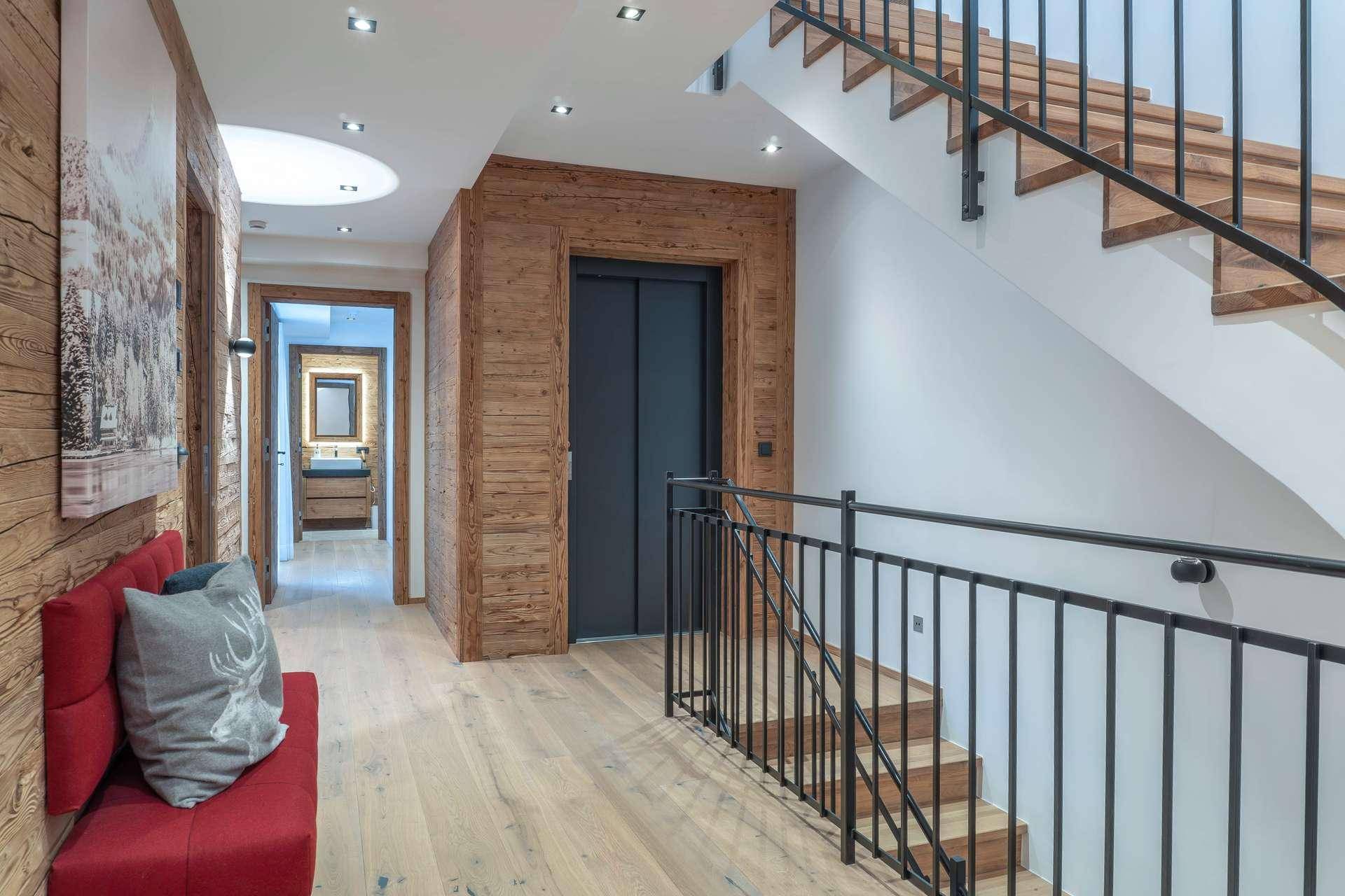 Heller Flur mit eleganter Holztreppe, Aufzug und modernen Holzwänden.