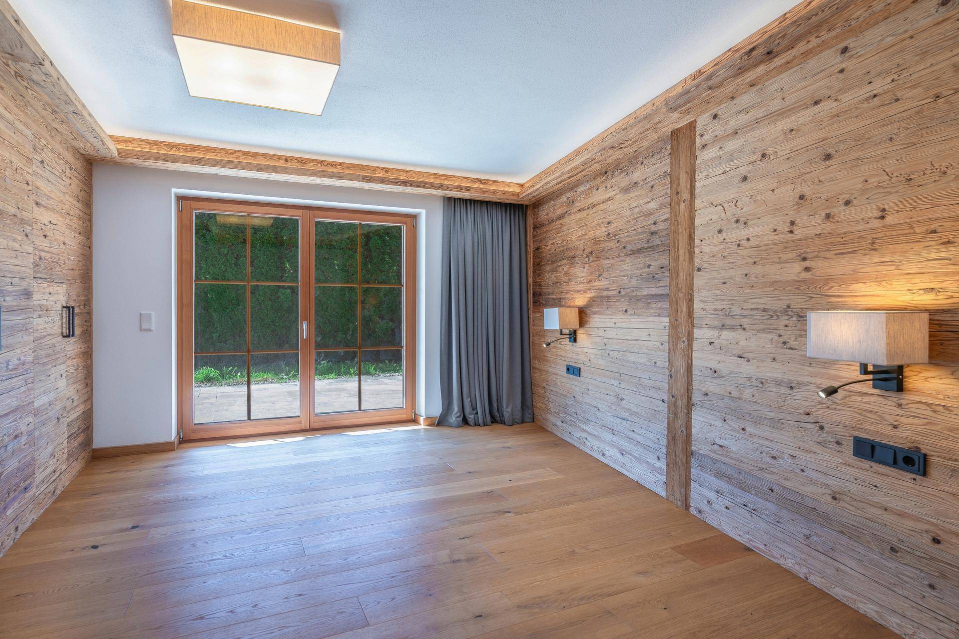 Geräumiges Zimmer mit Holzwänden, Parkettboden und Zugang zu einem Außenbereich.