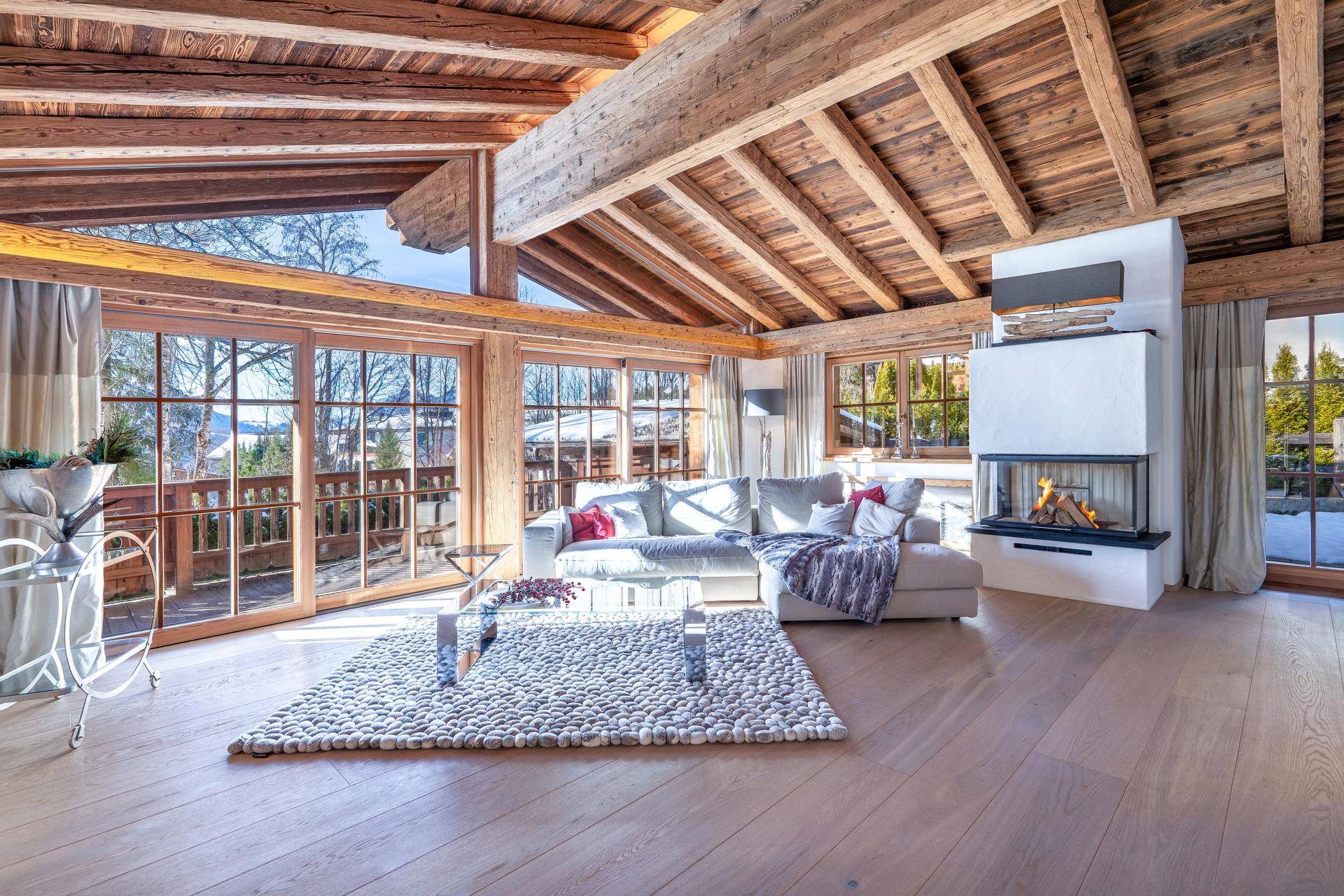 Geräumiges Wohnzimmer mit Kamin, Holzbalken und Panoramafenstern mit Bergblick.