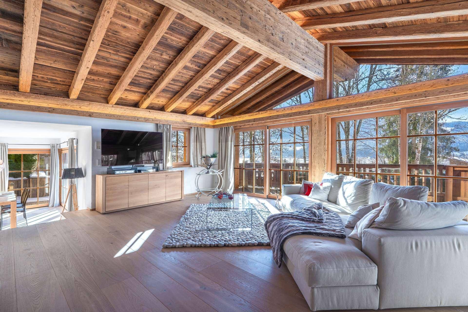 Helles Wohnzimmer mit Holzbalkendecke, großen Fenstern und Panoramablick auf die Berge.