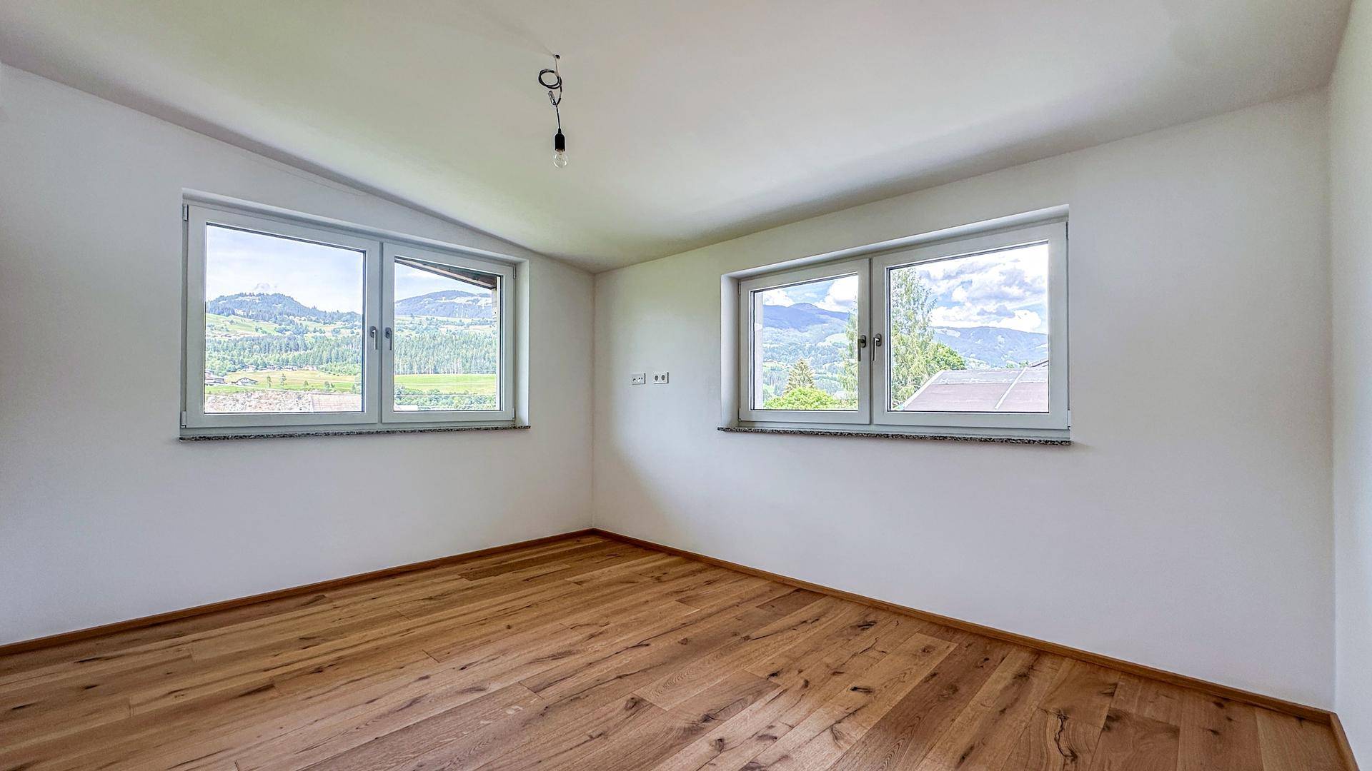 Helles Schlafzimmer mit Holzboden und zwei Fenstern, die einen schönen Blick auf die Landschaft ermöglichen.