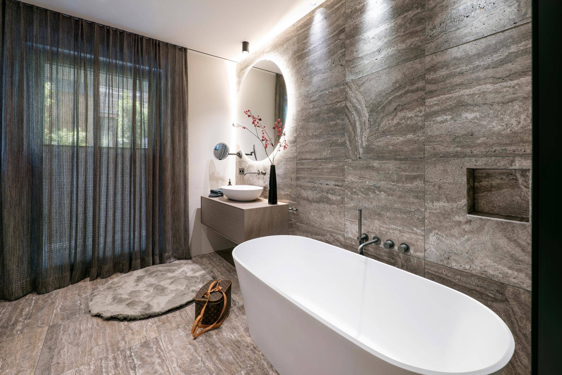 Luxuriöses Badezimmer mit freistehender Badewanne, modernem Waschtisch und Natursteinfliesen.