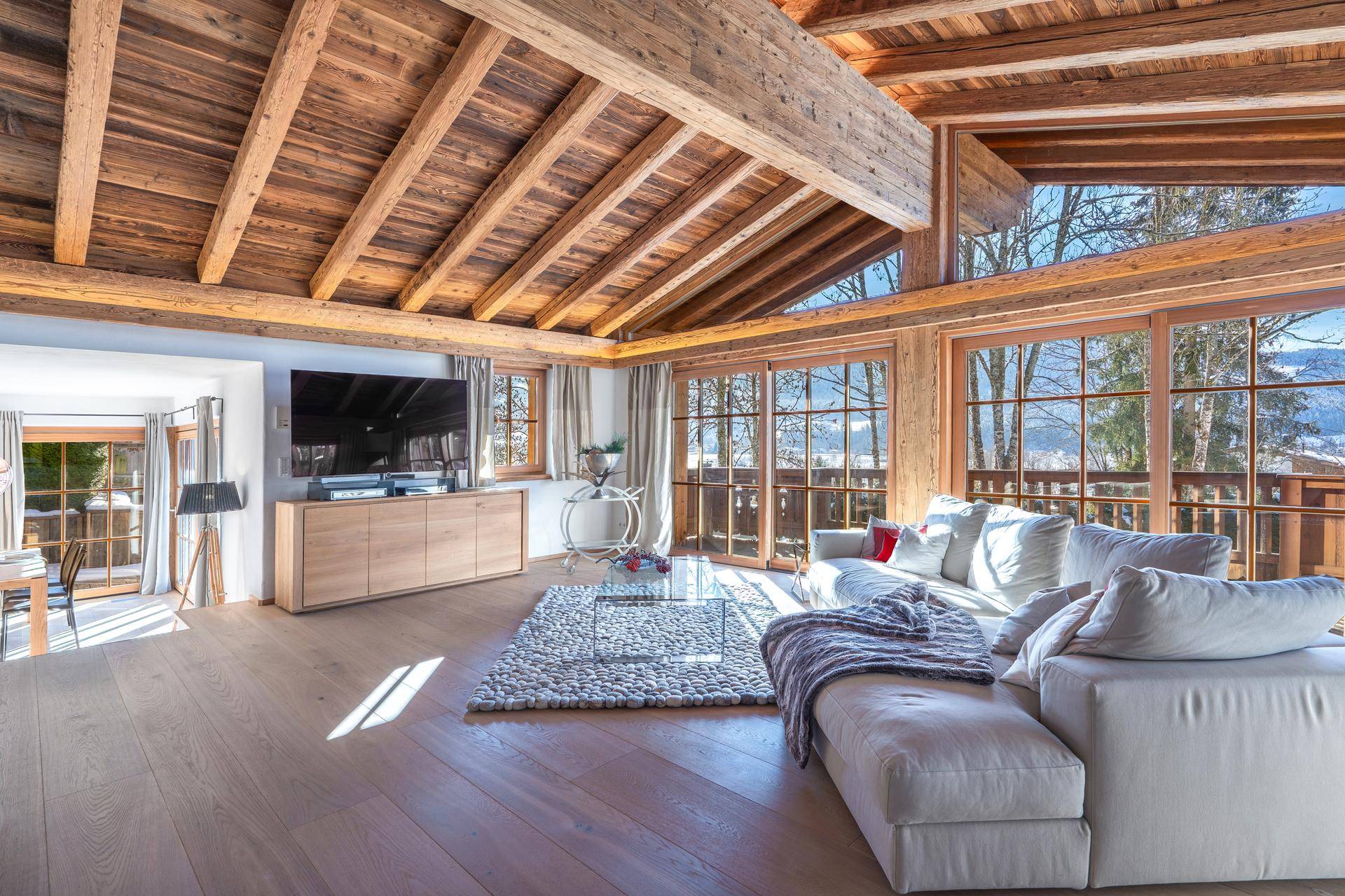 Helles Wohnzimmer mit hohen Holzdecken, großen Fenstern und modernem Sofa.