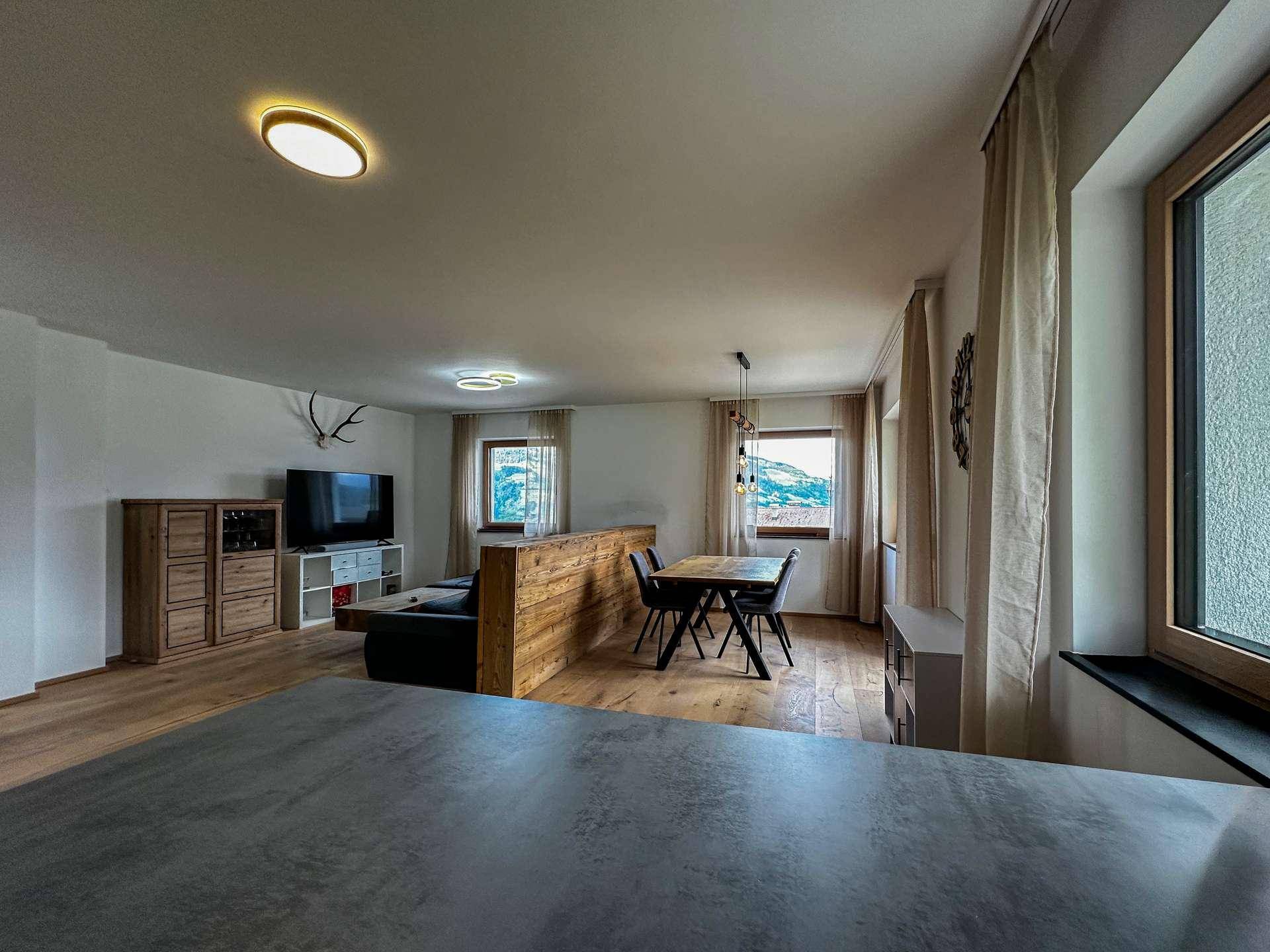 Offener Wohn- und Essbereich mit Holzboden, moderner Einrichtung und Panoramablick auf die Berge.