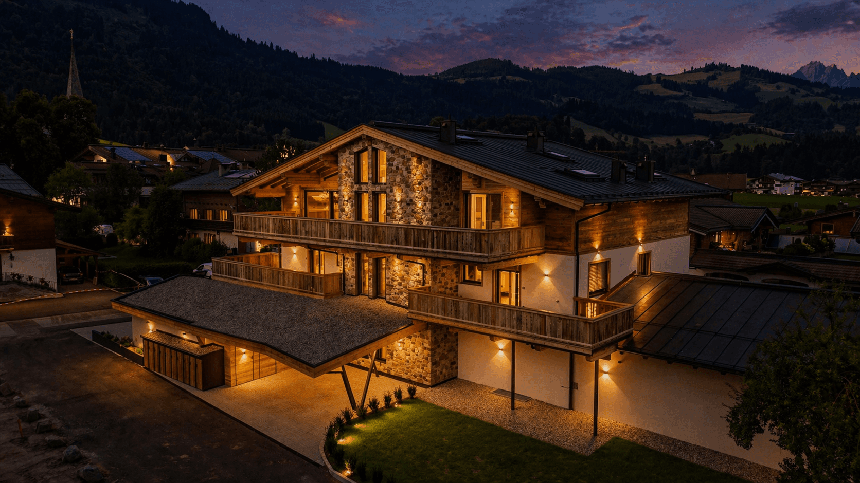 Luxuriöses Chalet im alpinen Stil mit beleuchteter Fassade und Bergblick bei Nacht.