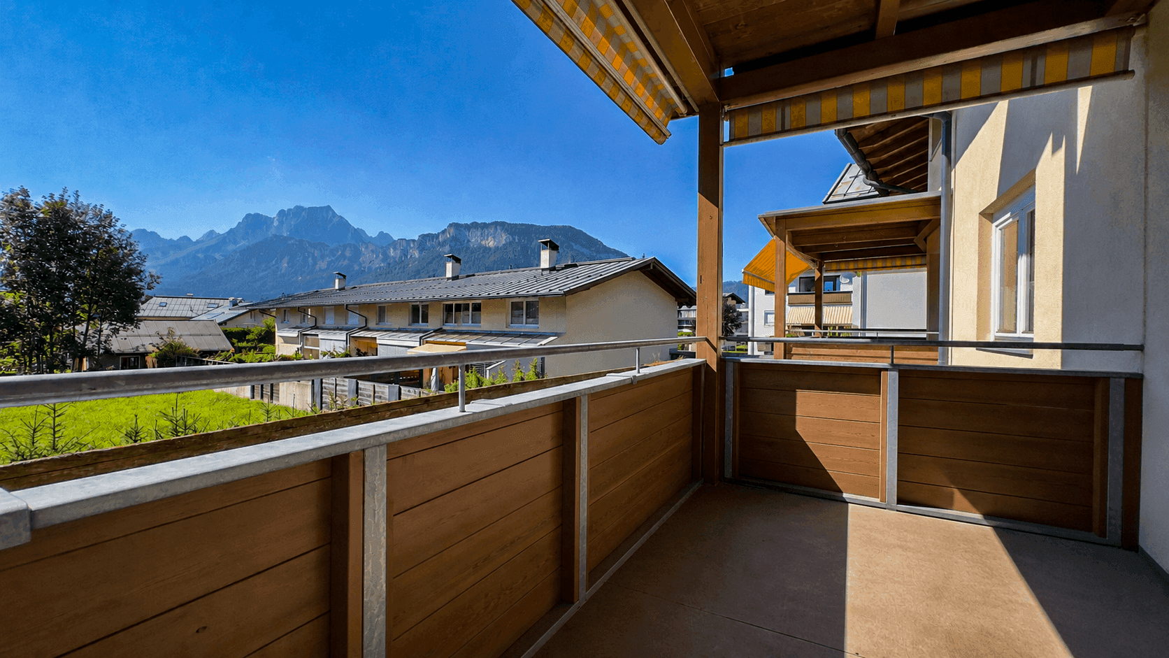 Geräumiger Balkon mit Holzelementen und Markise, bietet einen weiten Bergblick und viel Sonne.
