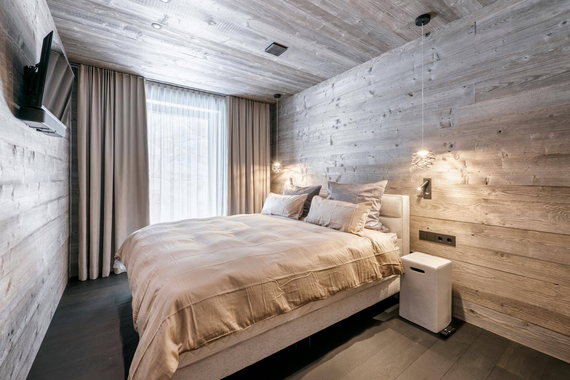 Gemütliches Schlafzimmer im alpinen Stil mit Holzwänden, Holzbalkendecke und großem Doppelbett.