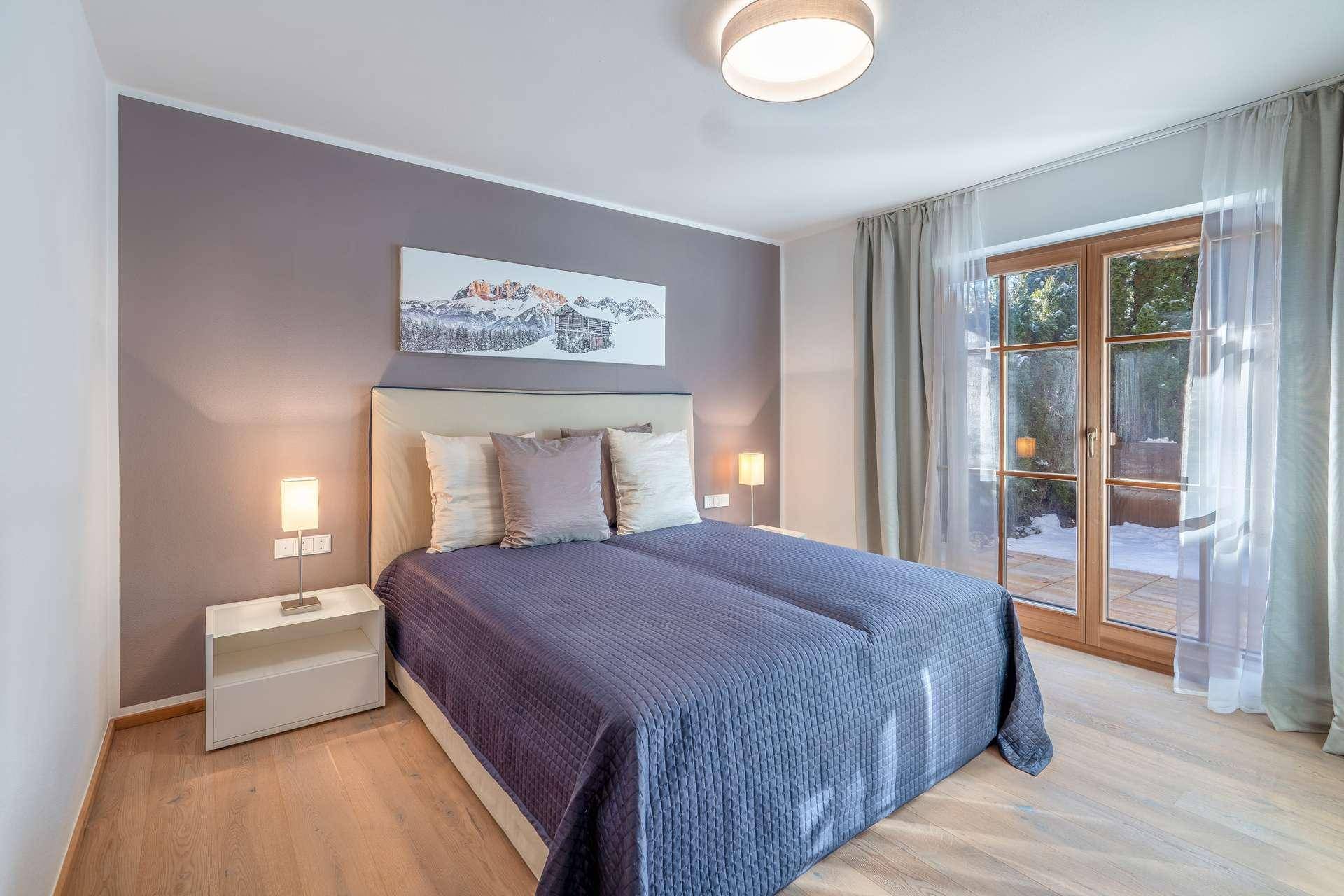 Modernes Schlafzimmer mit Doppelbett, Holzboden und Zugang zu einem sonnigen Außenbereich.