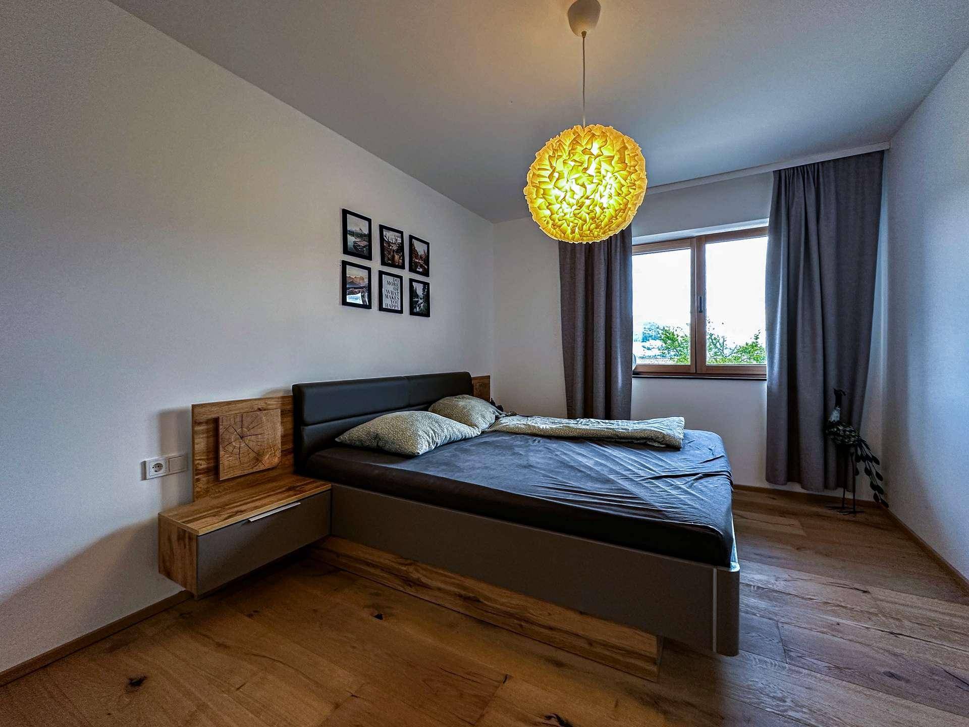Schlafzimmer mit Holzboden, modernem Bett und einem Fenster, das viel Tageslicht hereinlässt.