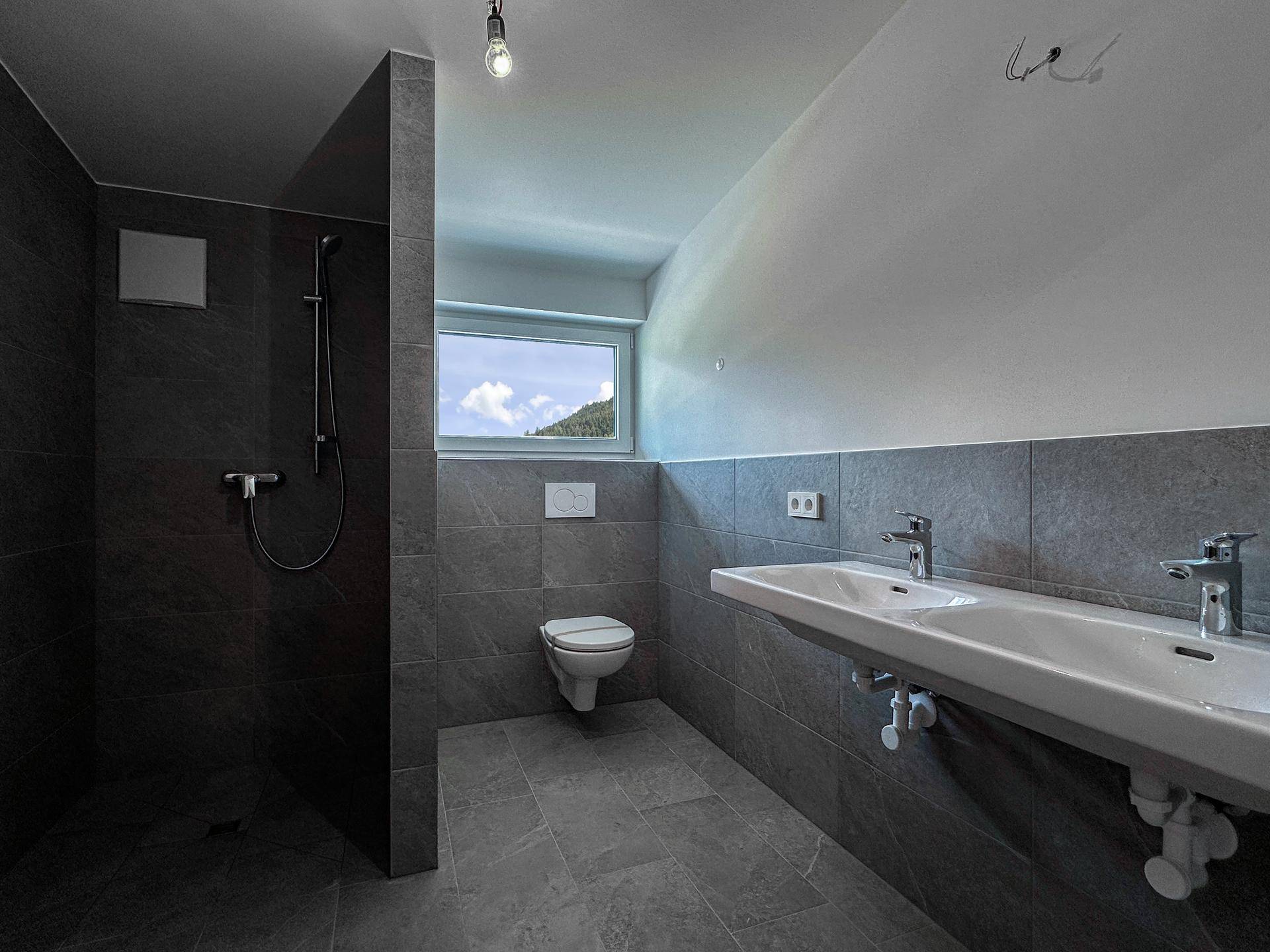 Modernes Badezimmer mit dunklen Fliesen, begehbarer Dusche, Doppelwaschbecken und Fenster.