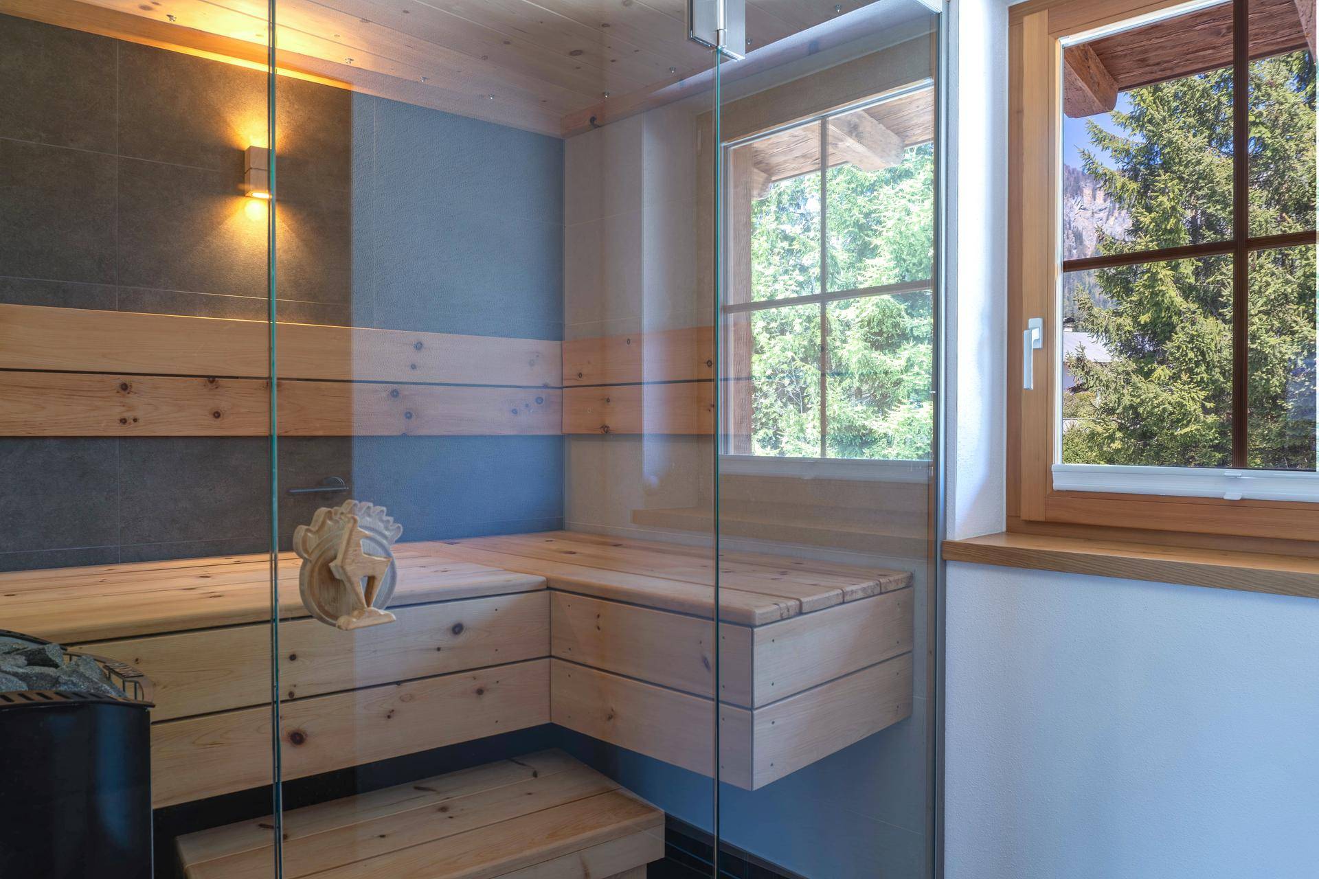 Private Sauna mit Holzverkleidung, Glasfront und Fenster mit Blick in die Natur.