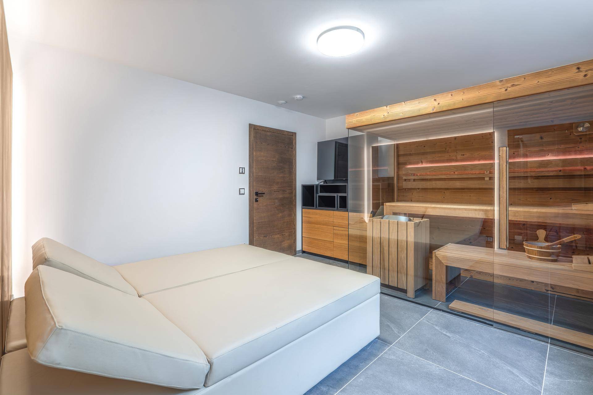 Entspannungsbereich mit bequemer Liege und moderner Sauna mit Glasfront.