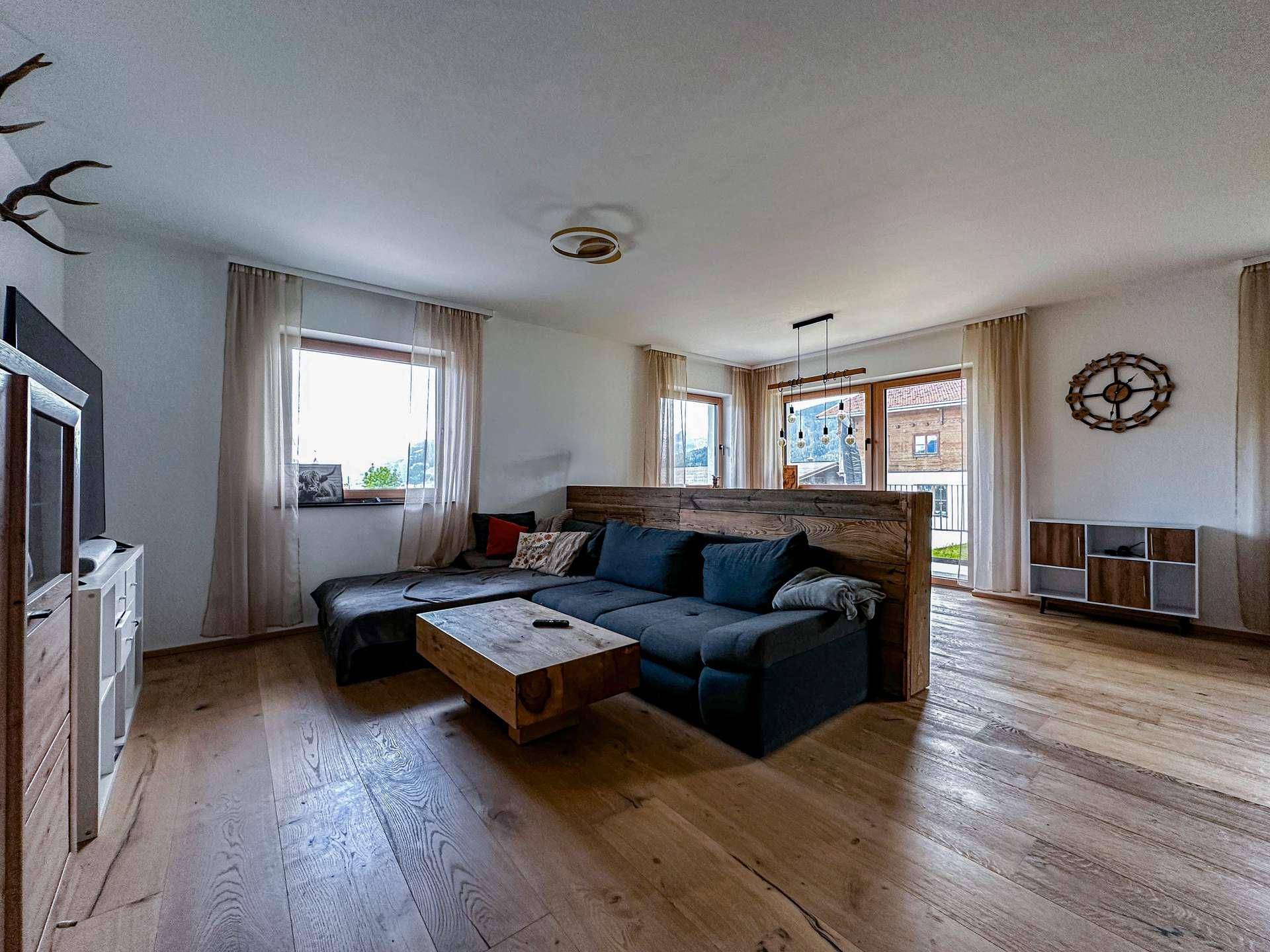 Gemütliches Wohnzimmer mit dunklem Sofa, Holztisch und Blick auf die umliegende Berglandschaft.
