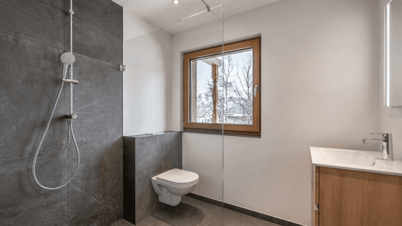 Modernes Badezimmer mit begehbarer Dusche, dunklen Fliesen und Fenster.