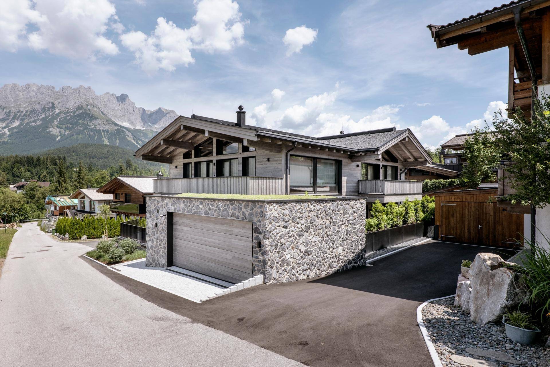 Modernes Chalet mit Steinfassade, Doppelgarage und Bergblick in alpiner Umgebung.