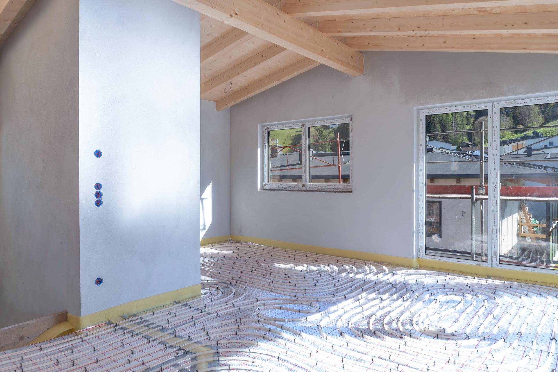 Raum im Rohbau mit sichtbaren Fußbodenheizungsrohren und Holzbalkendecke, bereit für den weiteren Ausbau.