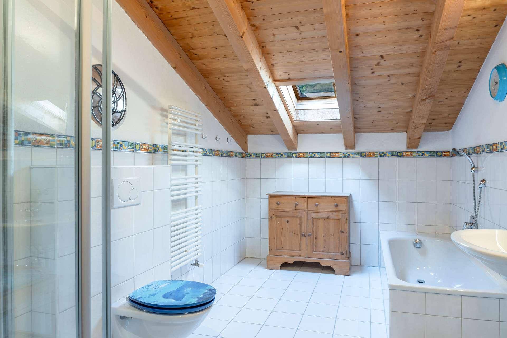 Badezimmer im Dachgeschoss mit Badewanne, Dusche, WC und Dachfenster für natürliches Licht.
