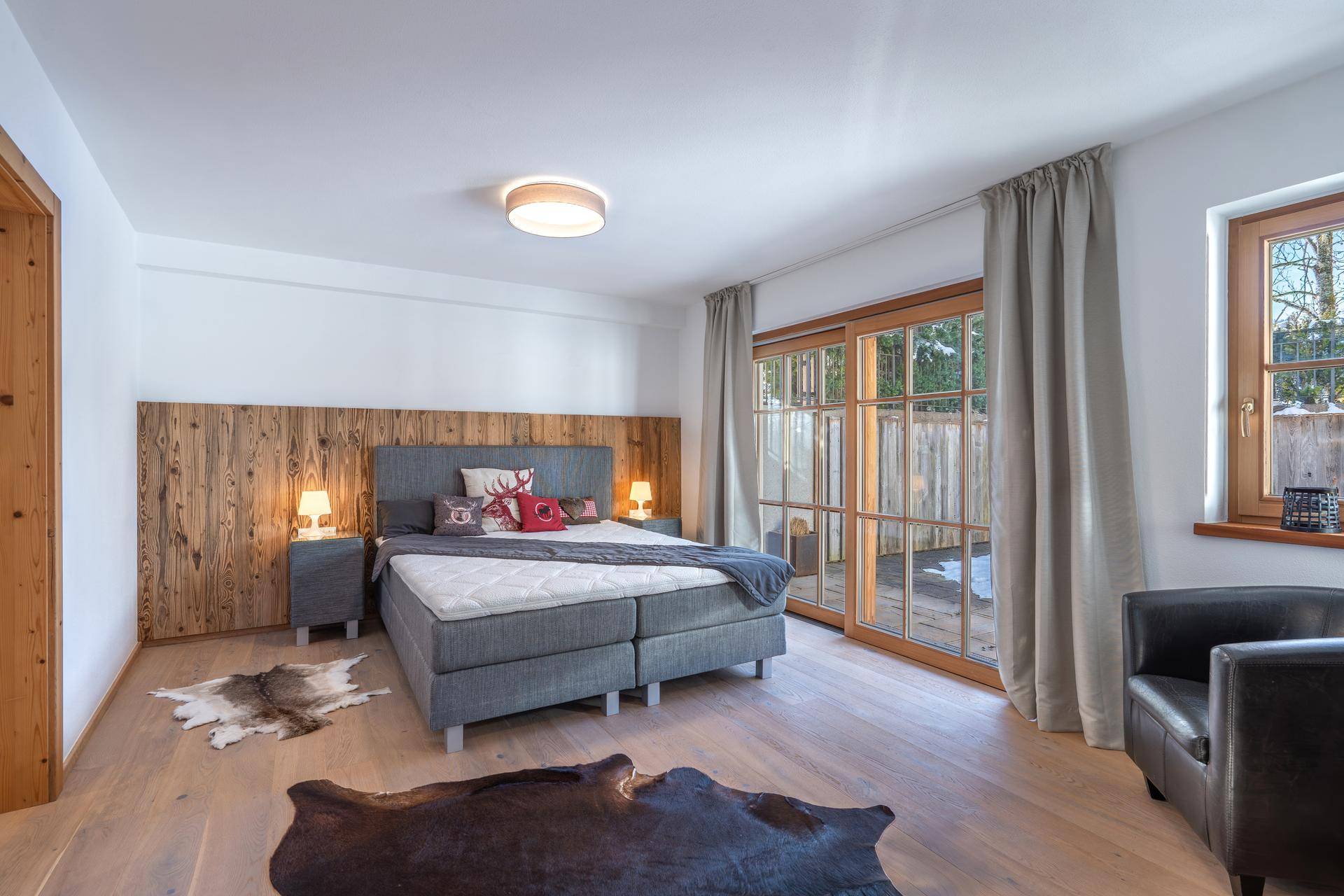 Schlafzimmer im alpinen Stil mit Holzwand, Doppelbett und Zugang zum Außenbereich.