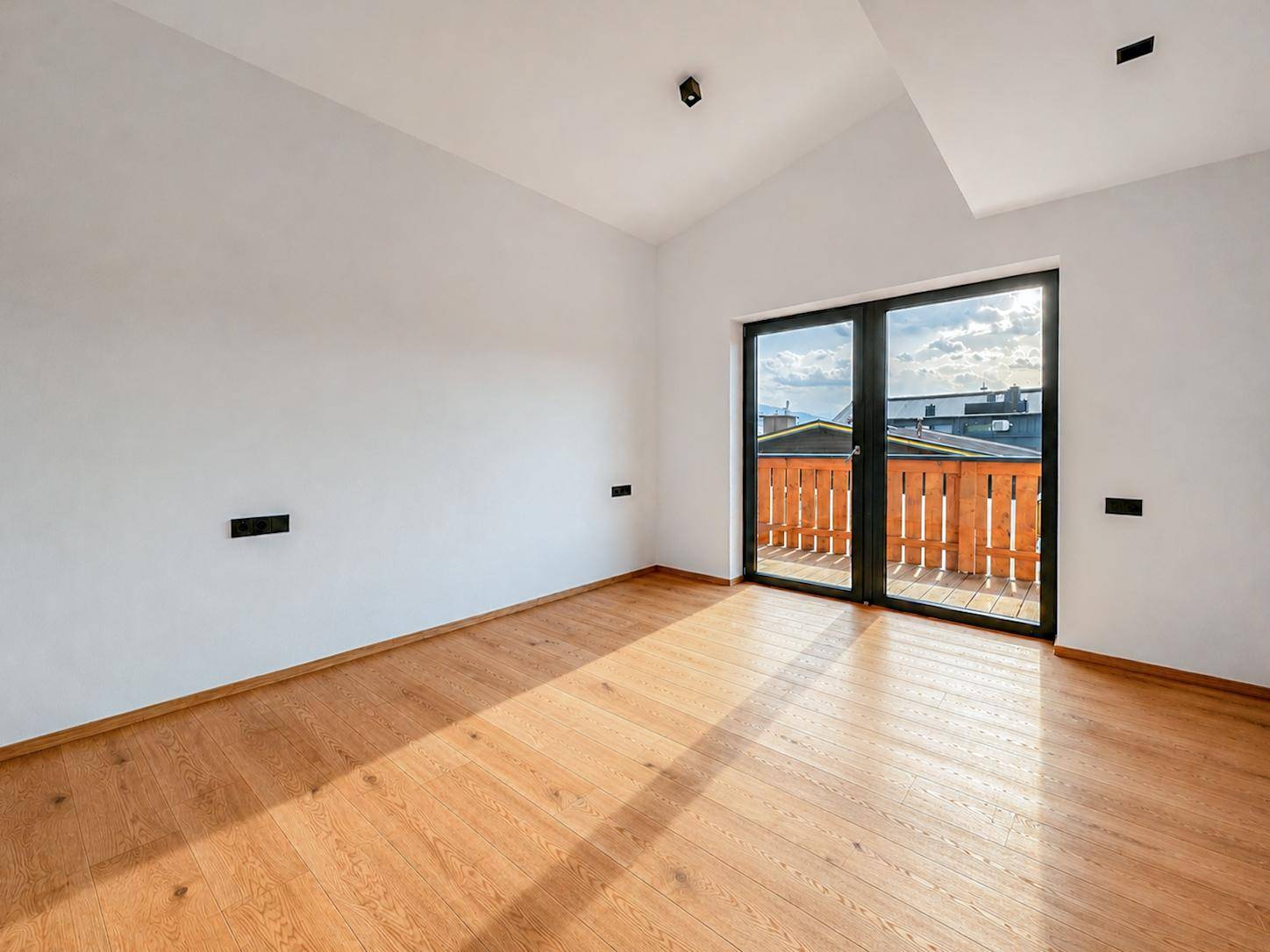 Heller Raum mit Holzboden und großem Schiebetürzugang zu einem Balkon.