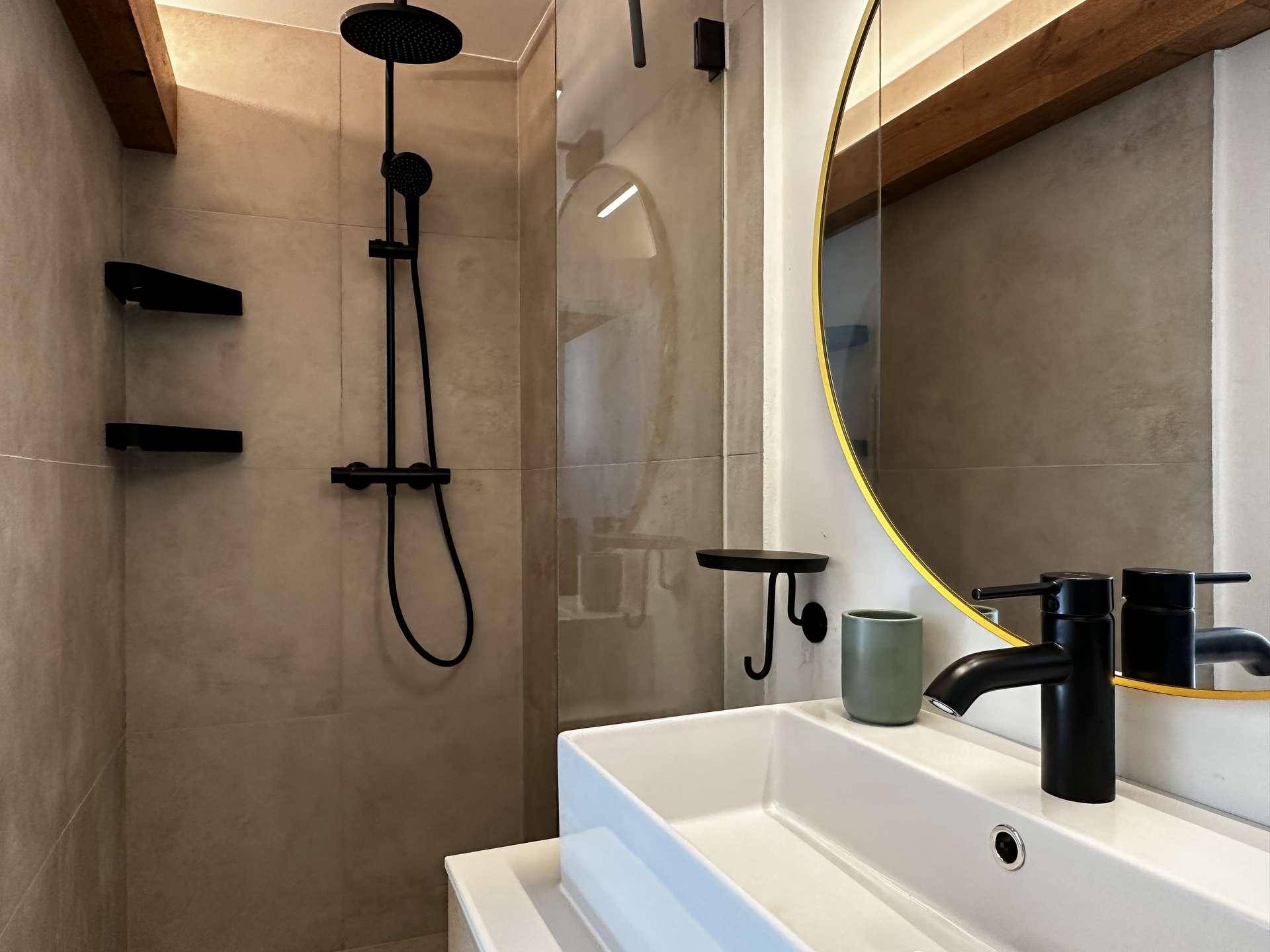 Modernes Badezimmer mit begehbarer Dusche, schwarzer Armatur und ovalem Spiegel.
