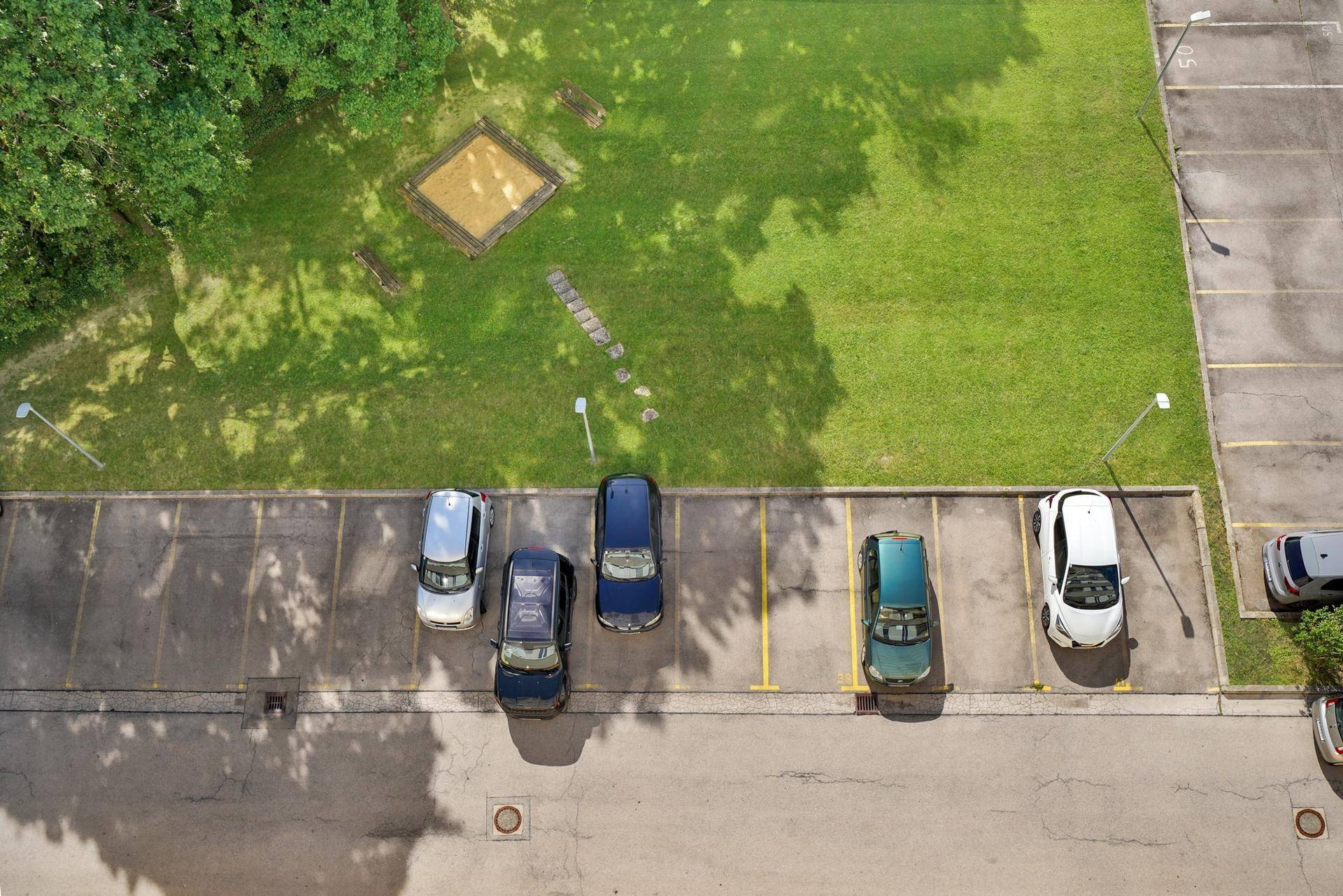 Vogelperspektive auf einen Parkplatz mit Autos und einer angrenzenden Grünfläche.