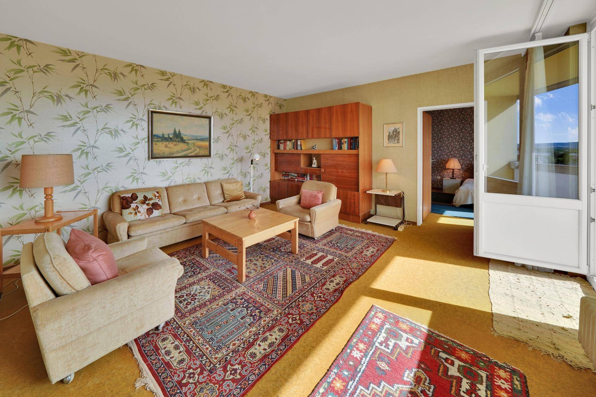 Gemütliches Wohnzimmer mit Sitzgelegenheiten, Teppichboden und Balkonzugang.