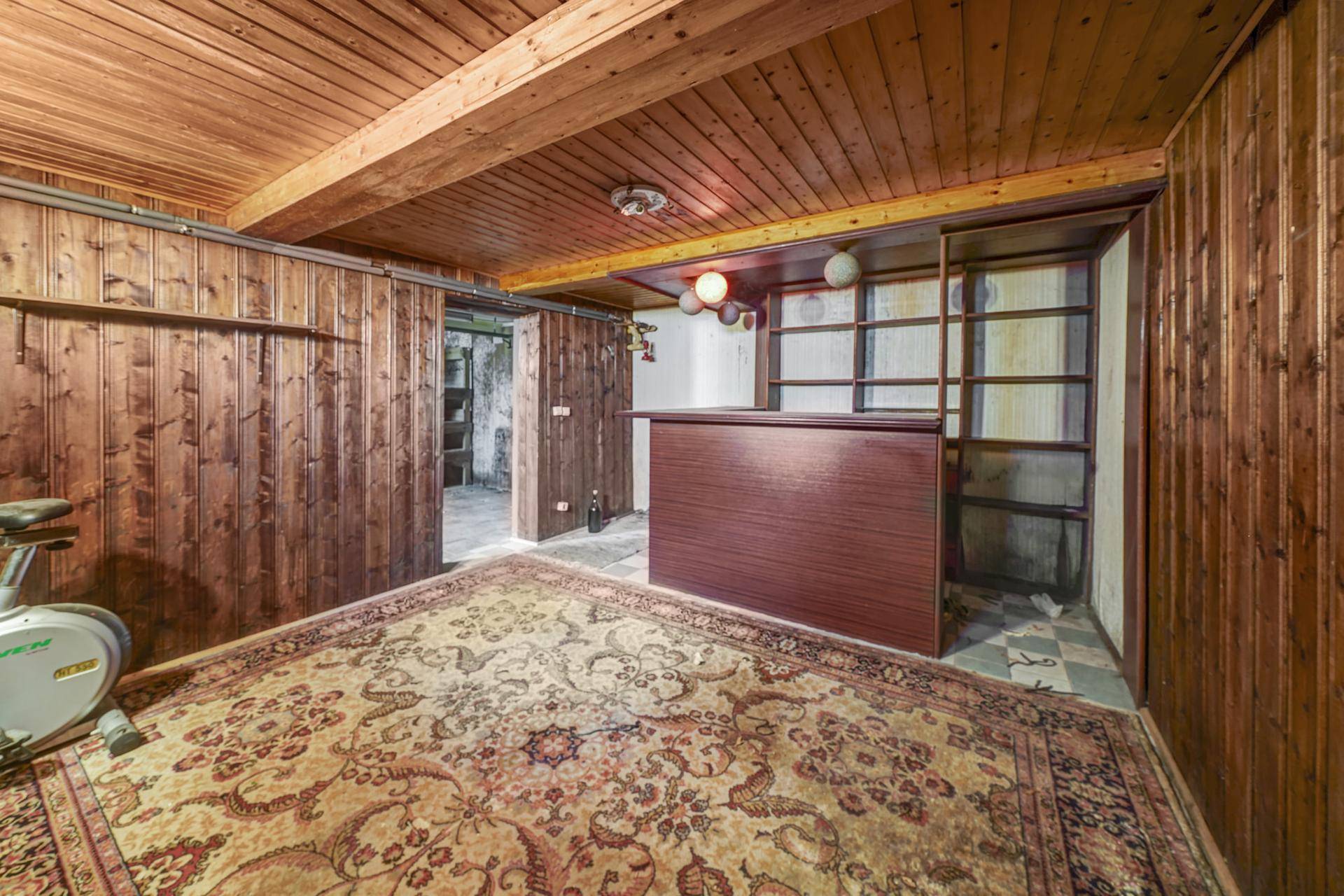 Rustikaler Hobbyraum im Keller mit Holzverkleidung, Teppich und kleiner Bar.