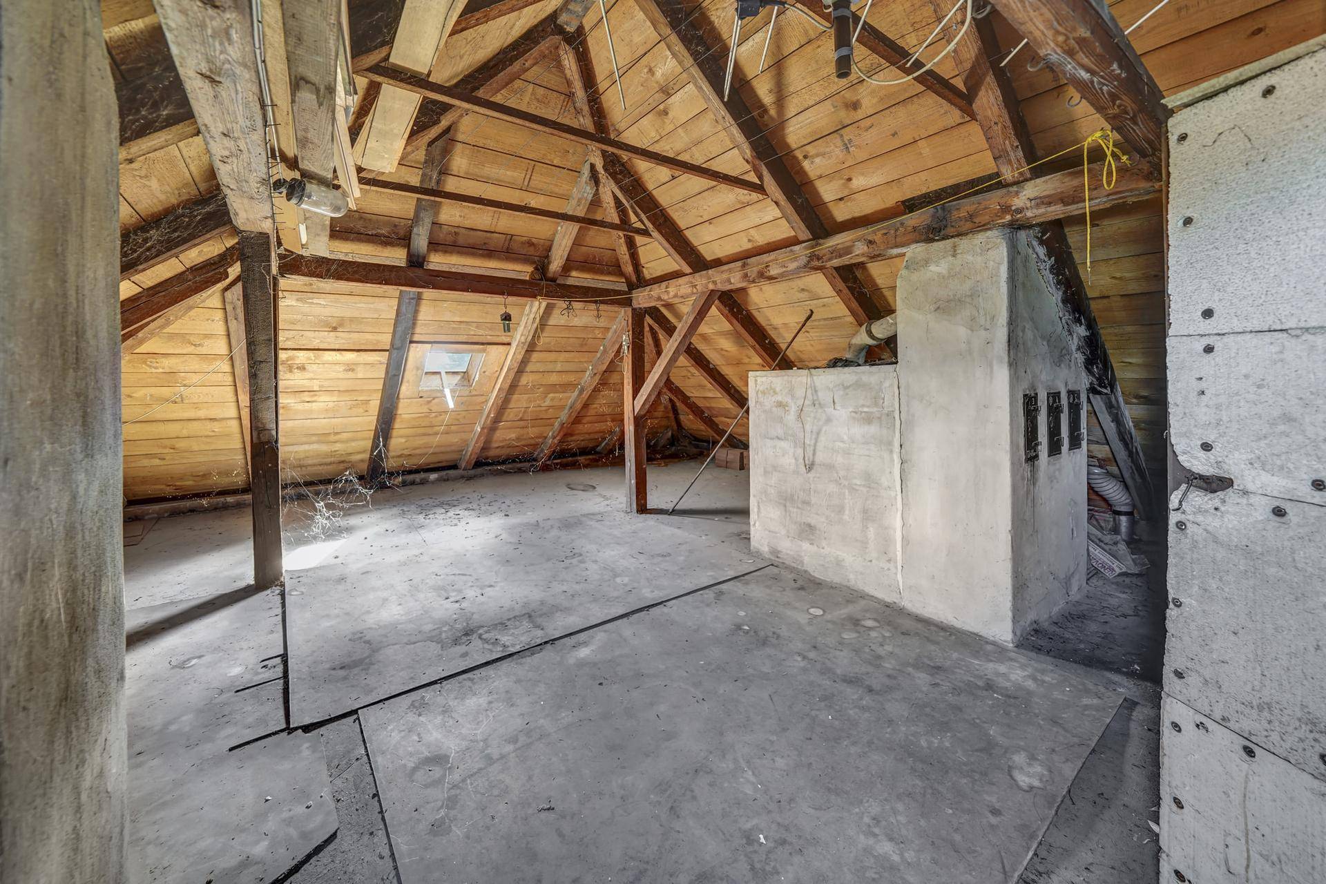 Unausgebauter Dachboden mit sichtbaren Holzbalken und Dachfenster, viel Potenzial.