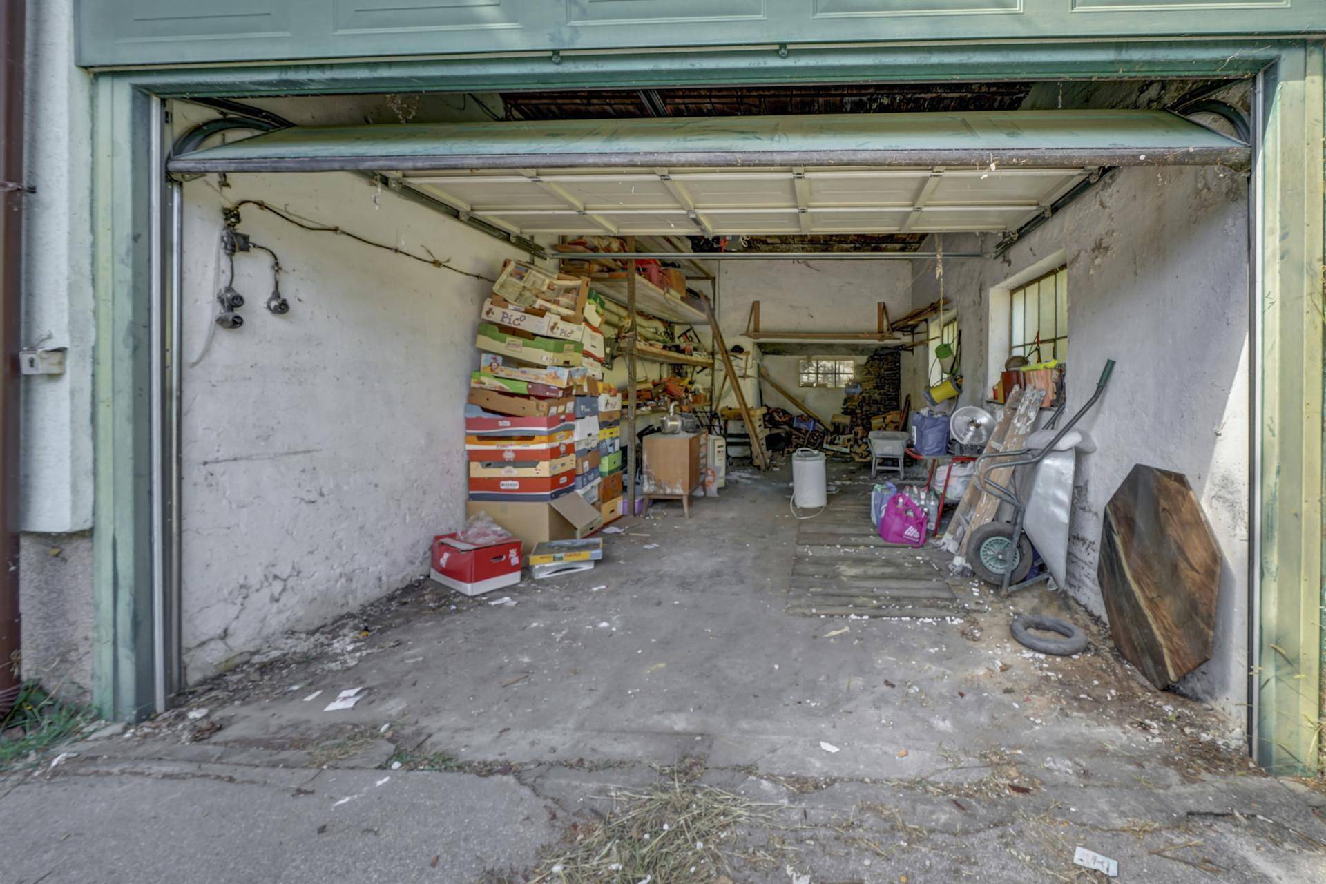 Geräumige Garage mit Betonboden und Lagerflächen, ideal für Fahrzeuge und Werkzeuge.