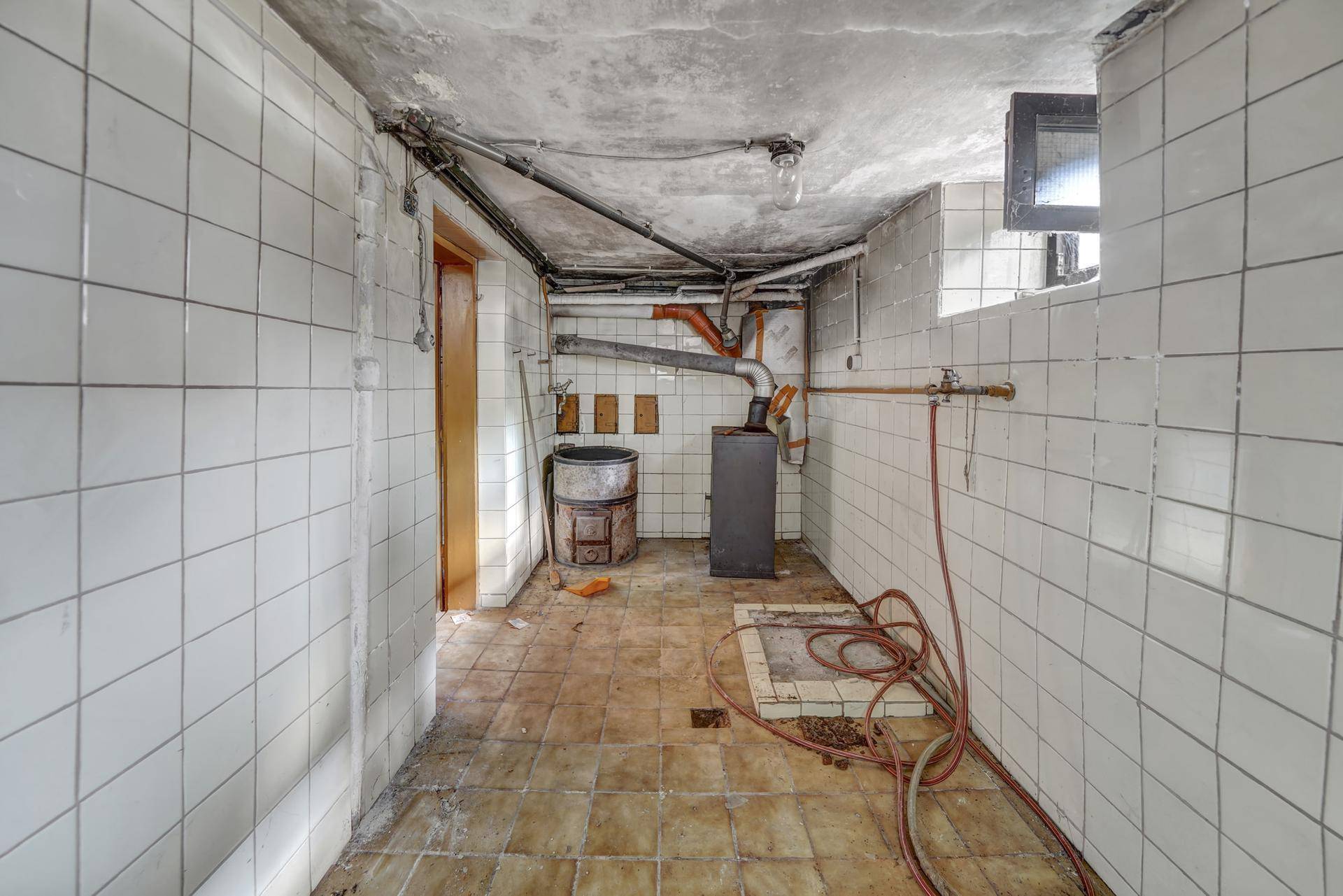 Gefliester Kellerraum mit altem Ofen und sichtbaren Rohren, als Heizraum genutzt.