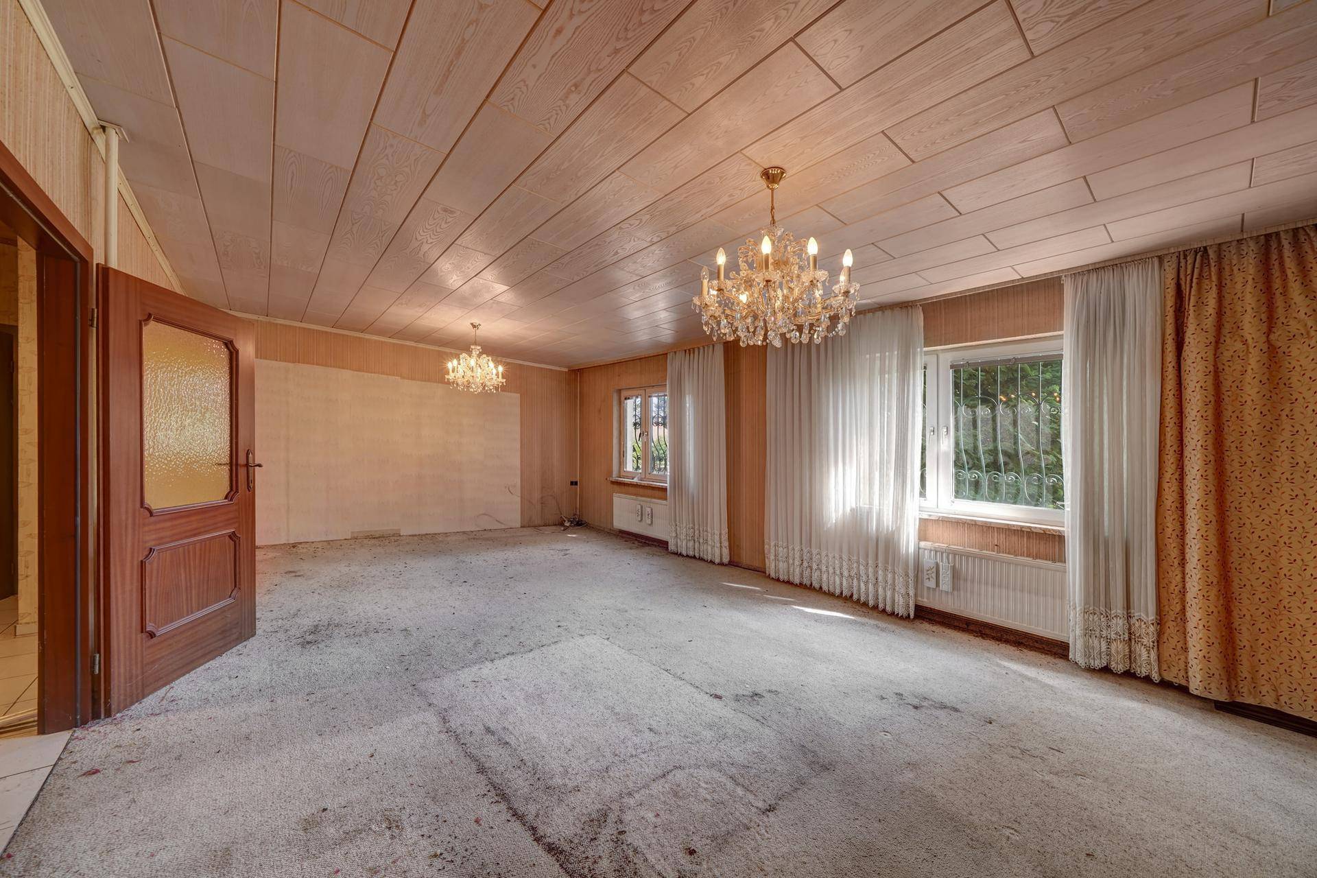 Geräumiges Wohnzimmer mit Teppichboden, Holzdecke und zwei opulenten Kronleuchtern.