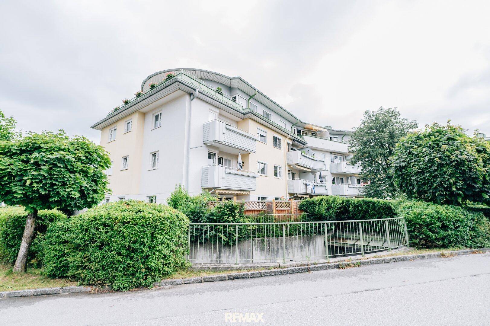 Ansicht eines modernen Mehrfamilienhauses mit mehreren Balkonen und gepflegter Grünanlage.