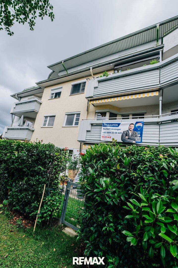 Fassade des Mehrfamilienhauses mit Balkonen, Markisen und einem großen Verkaufsplakat.