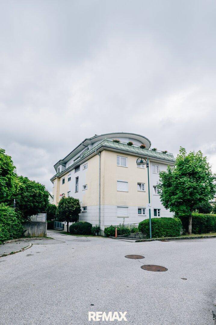 Ansicht des Mehrfamilienhauses von einer Straßenecke mit geschwungener Dachlinie und viel Grün.