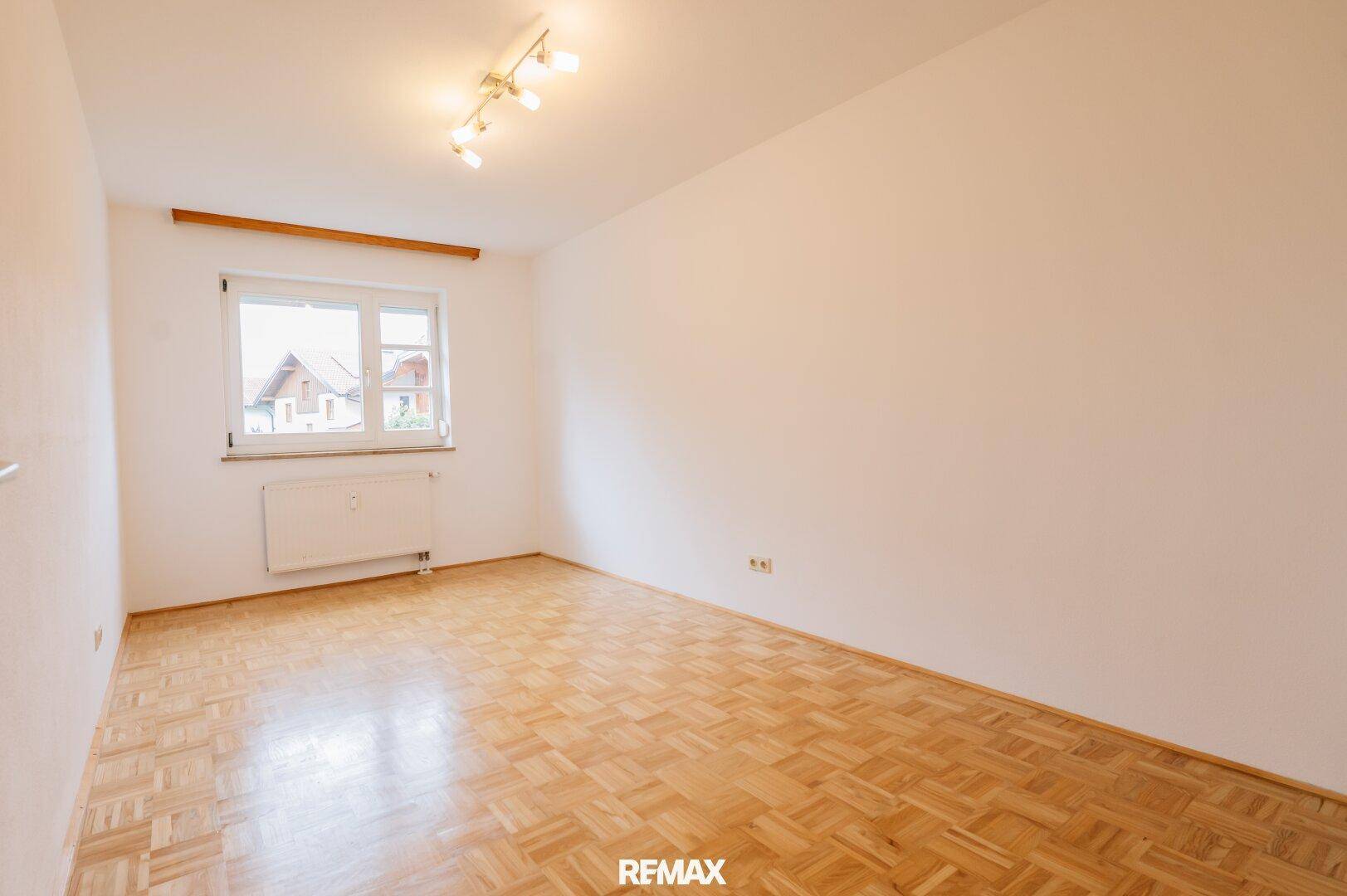 Helles Zimmer mit Parkettboden, weißen Wänden und einem Fenster mit Blick ins Grüne.