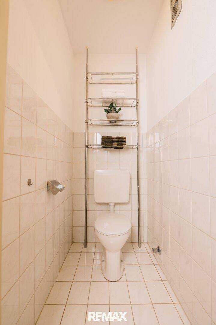Kleines Gäste-WC mit weißen Fliesen und einer einfachen Toilettenanlage.