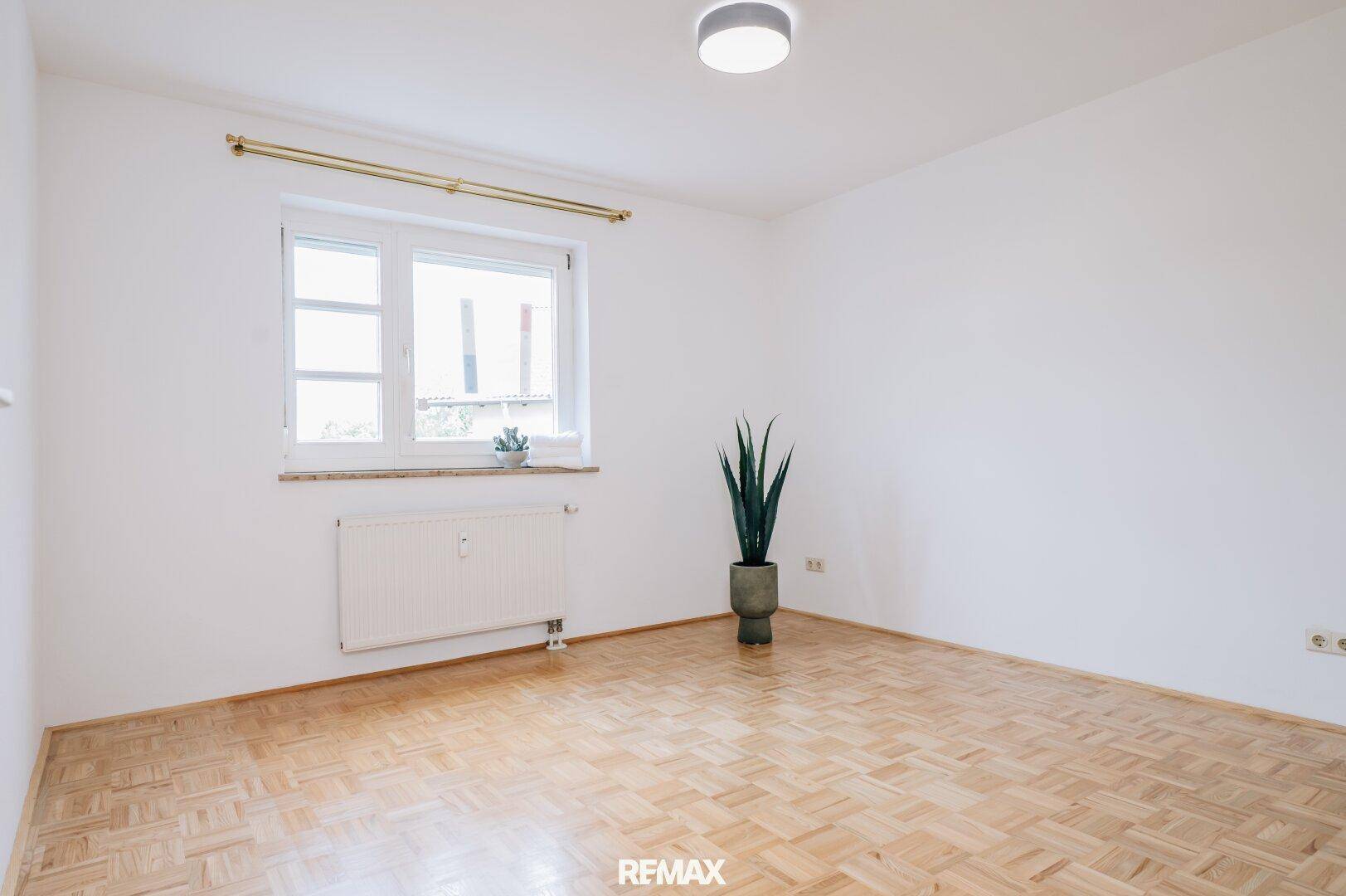 Helles Schlafzimmer mit Parkettboden, weißen Wänden und einem Fenster für natürliches Licht.