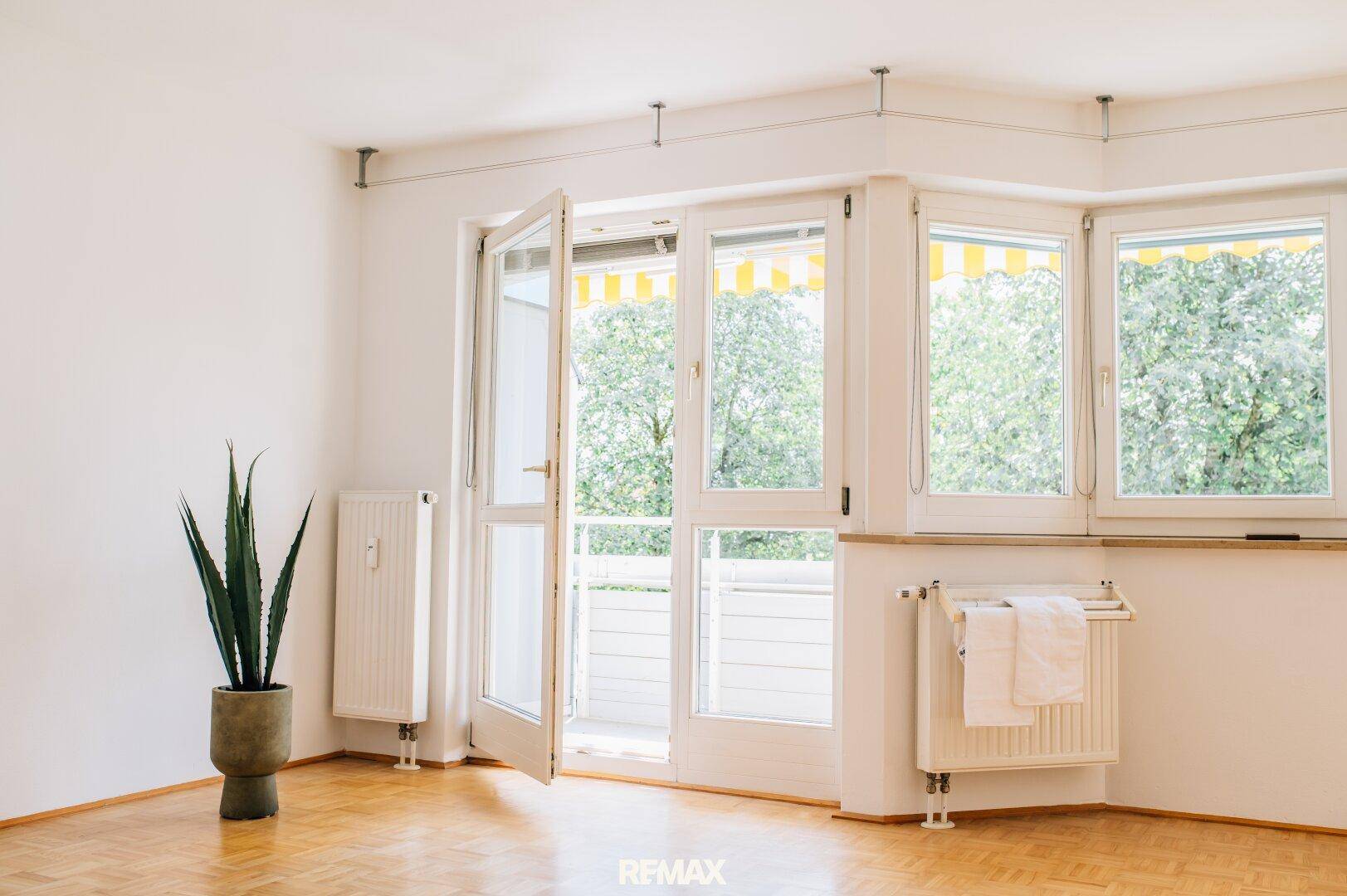 Lichtdurchflutetes Wohnzimmer mit Parkettboden und großen Fenstern, die zum Balkon führen.